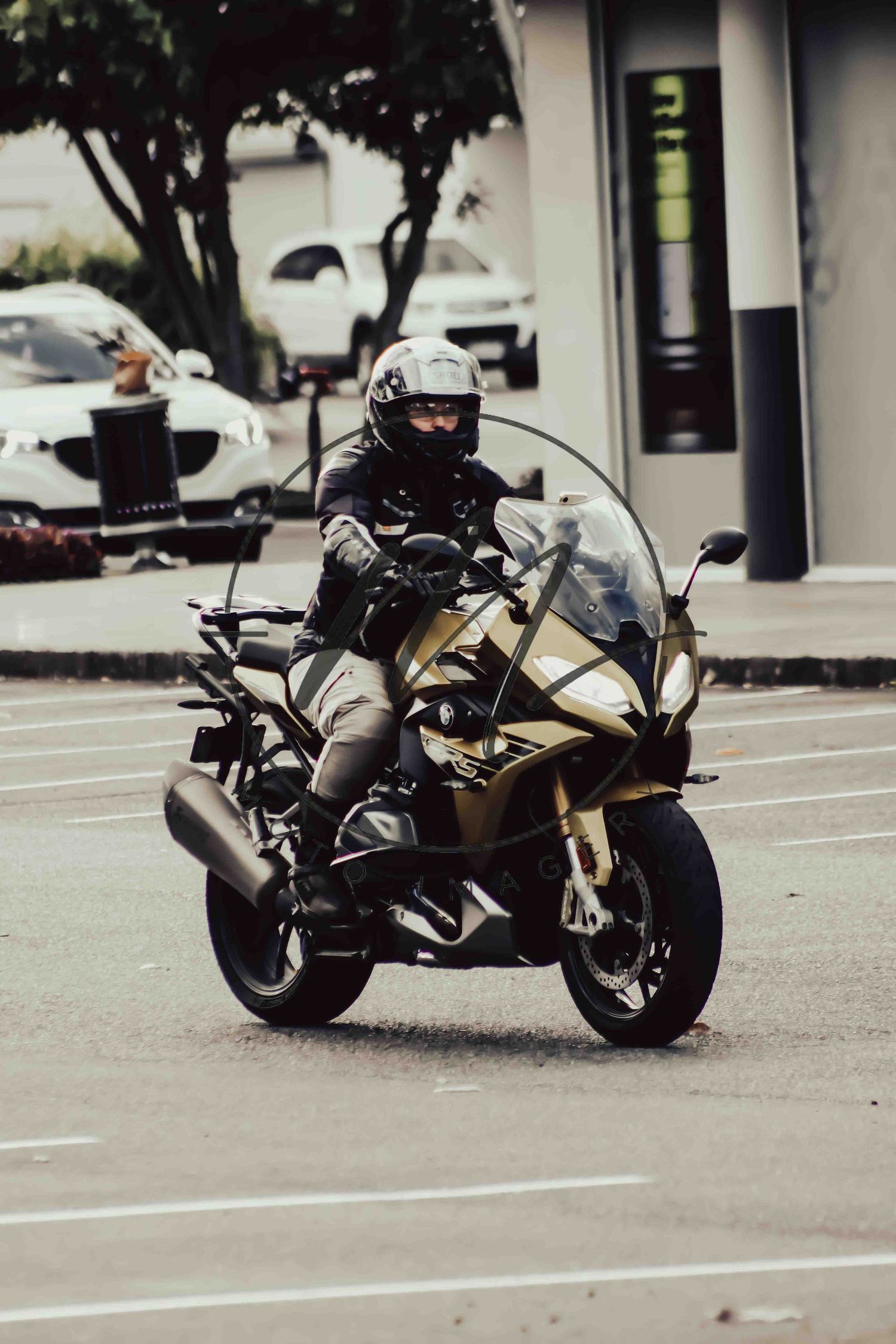 A rider in a white helmet navigates a gold BMW motorcycle through a parking lot.