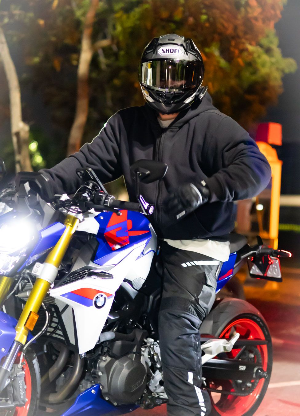 Motorcyclist on a colorful BMW sport bike with bright LED headlight in autumn setting.