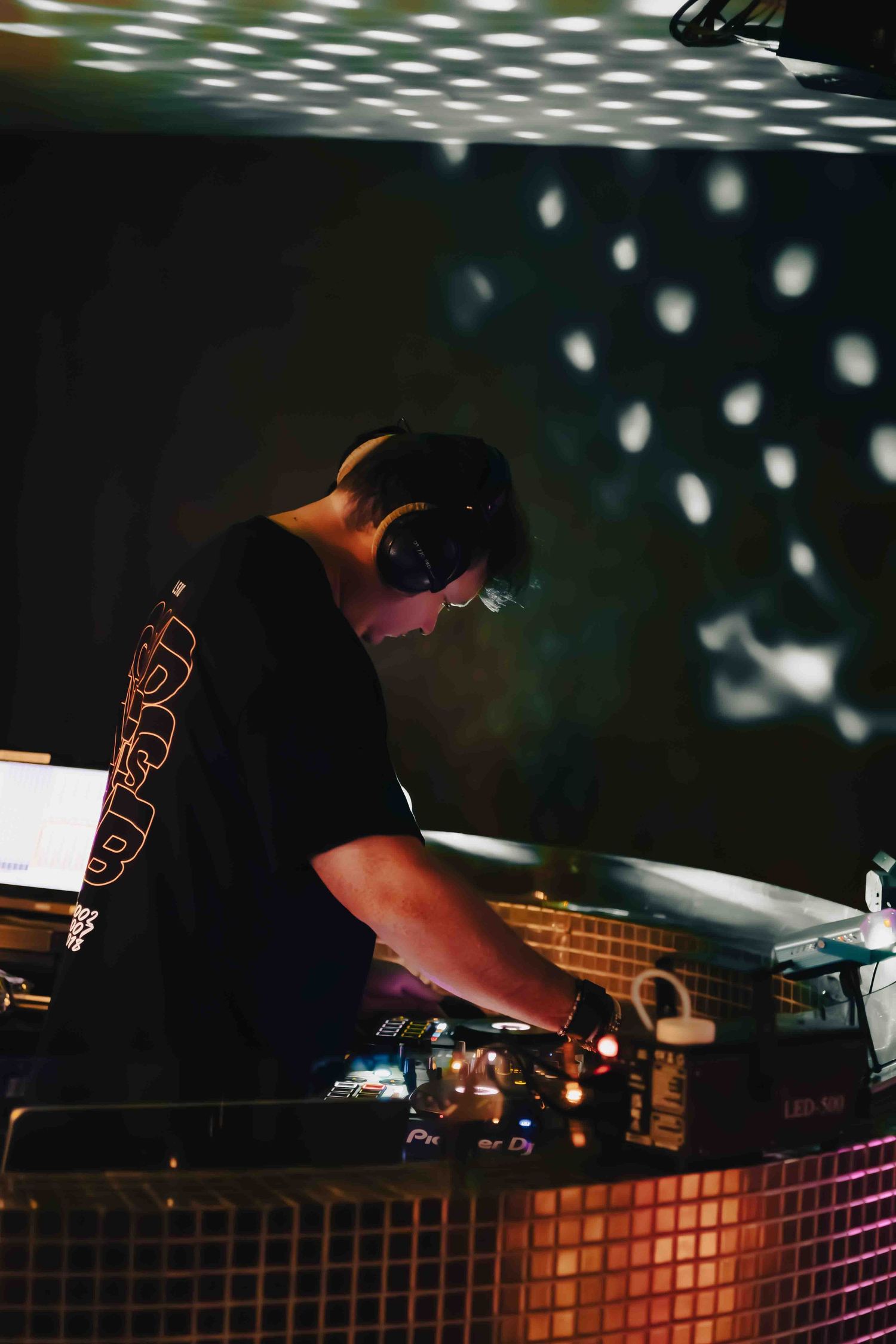 DJ mixing music at a dimly lit booth with scattered light effects.