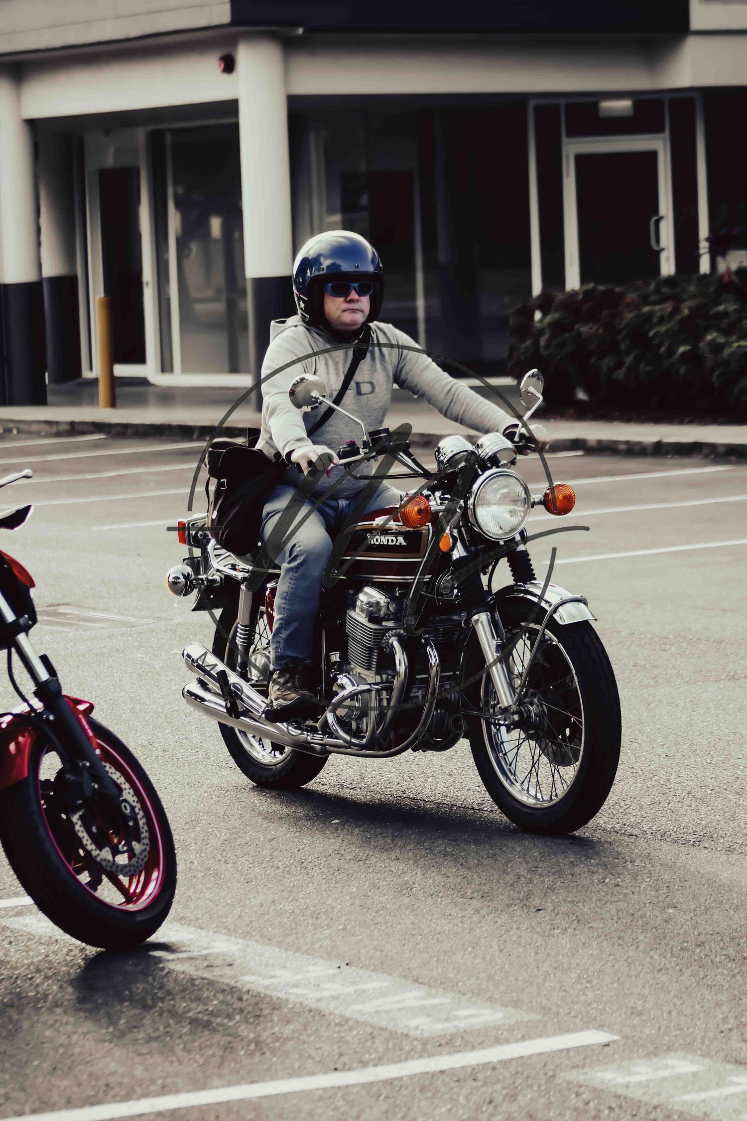 Man riding a classic Honda motorcycle wearing a blue helmet and jeans in a parking lot.