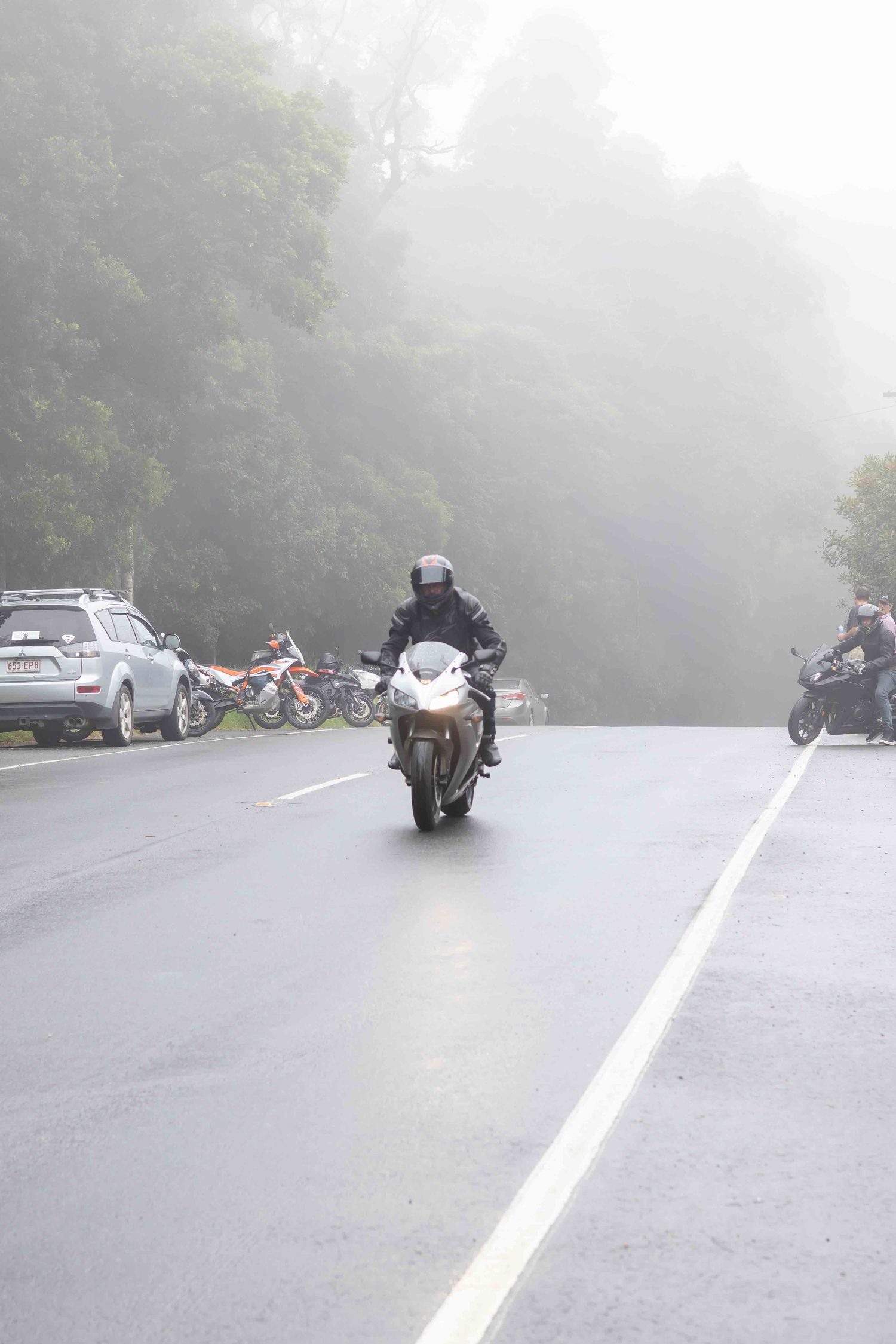 Multiple motorcycles parked and riding on a foggy mountain roadway.