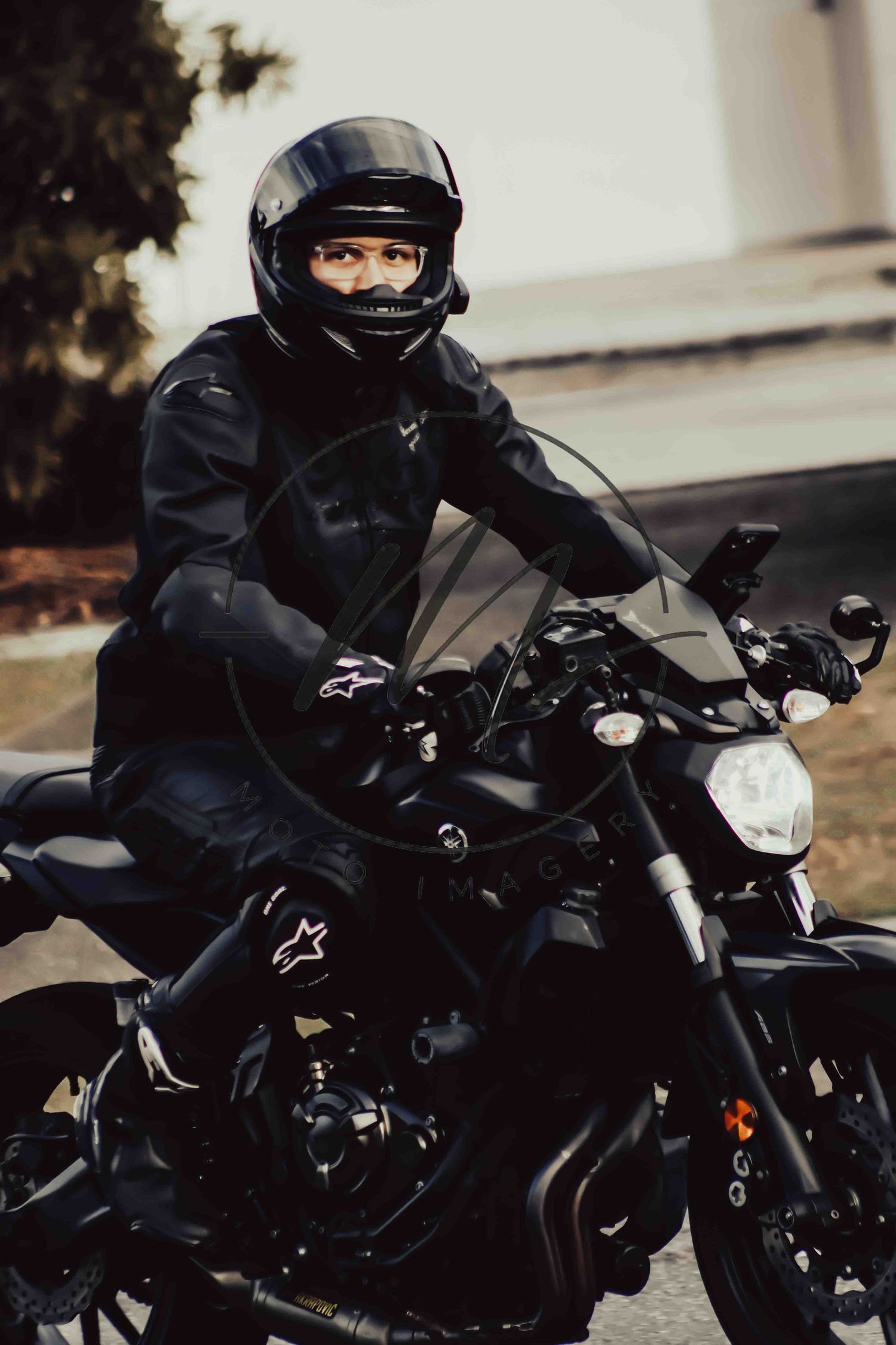 A motorcyclist in full black Alpinestars gear and helmet sits on a black motorcycle outdoors.