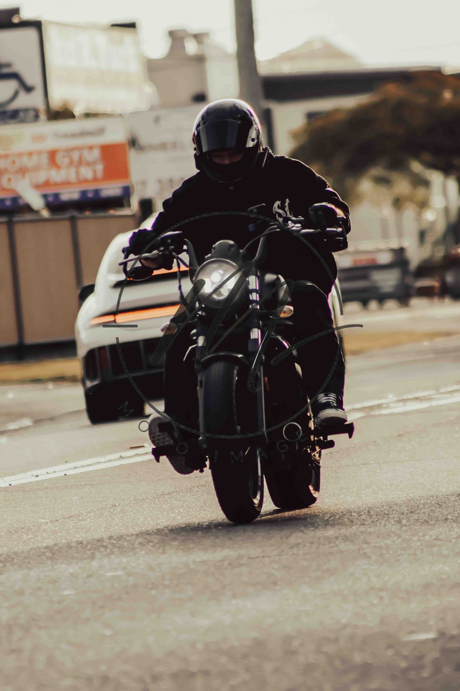 Rider in black helmet and jacket on a dark cruiser motorcycle traveling along a city street.