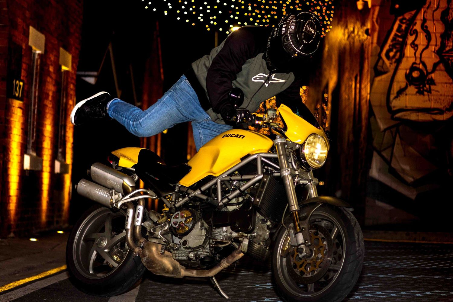 Row of motorcycles displayed under ambient string lights in an urban setting.