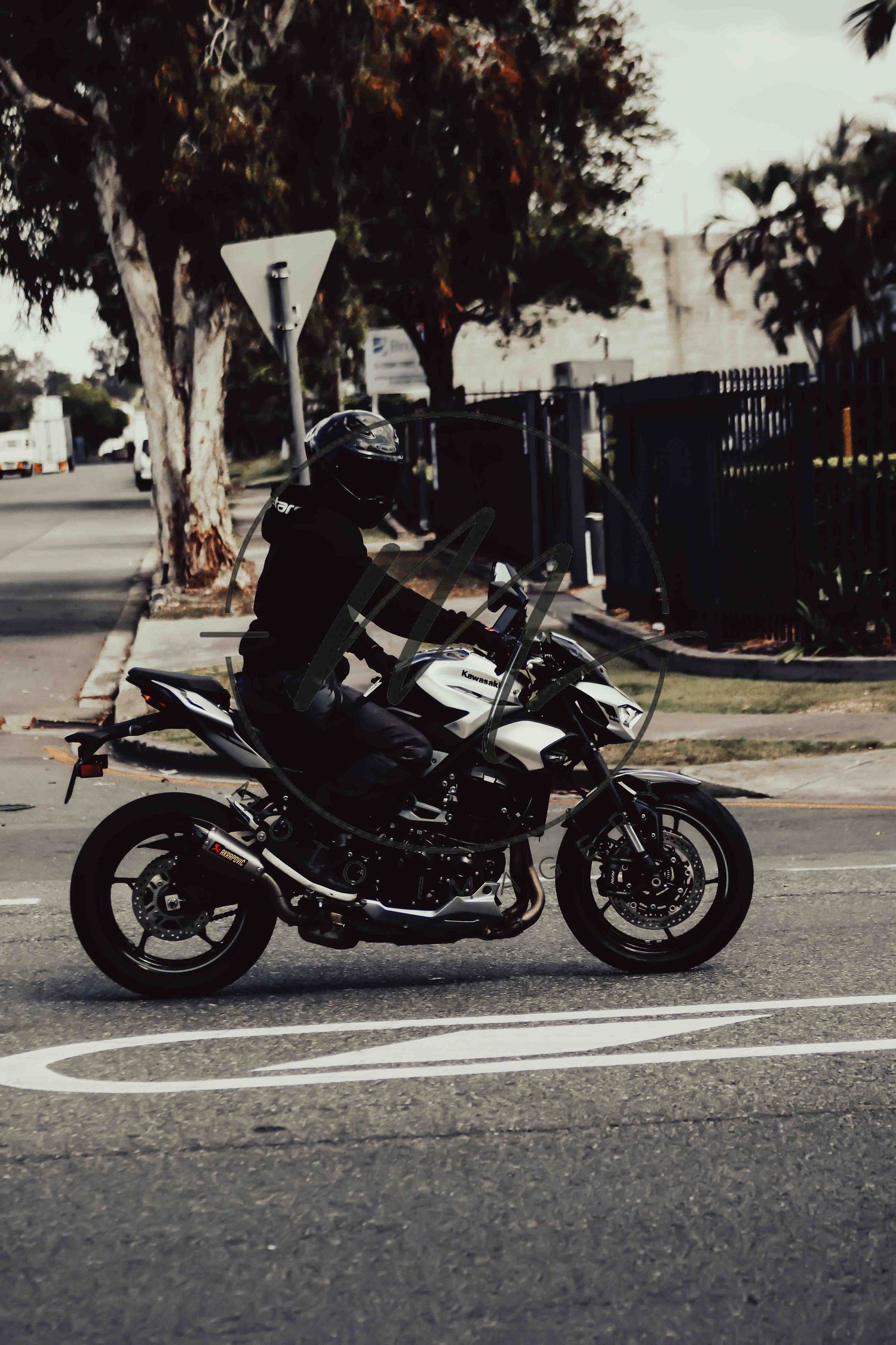 A motorcyclist in black gear and helmet rides a white and black sport motorcycle on an urban street.