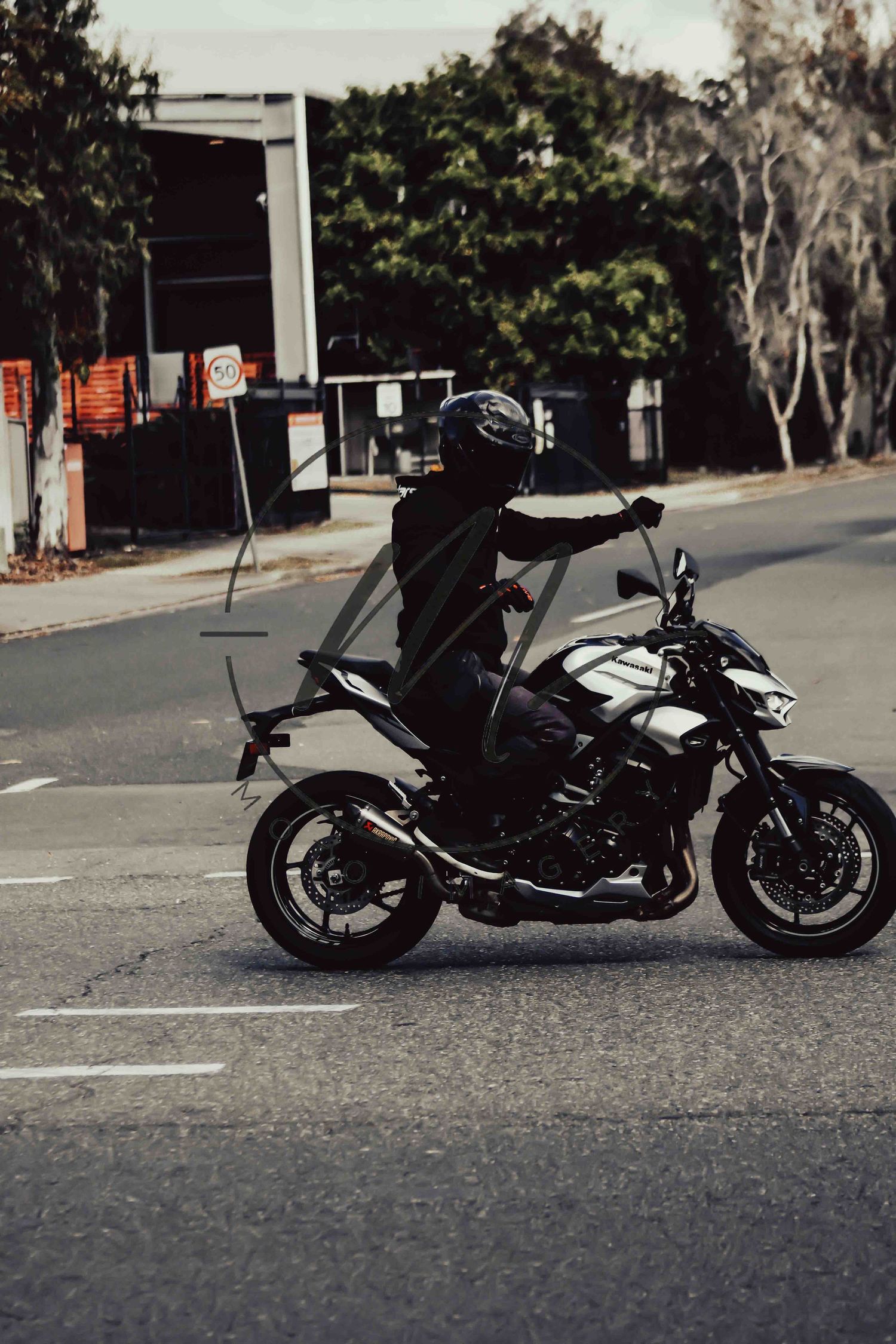 Motorcyclist in black gear and helmet riding a white and black motorcycle on a suburban road.