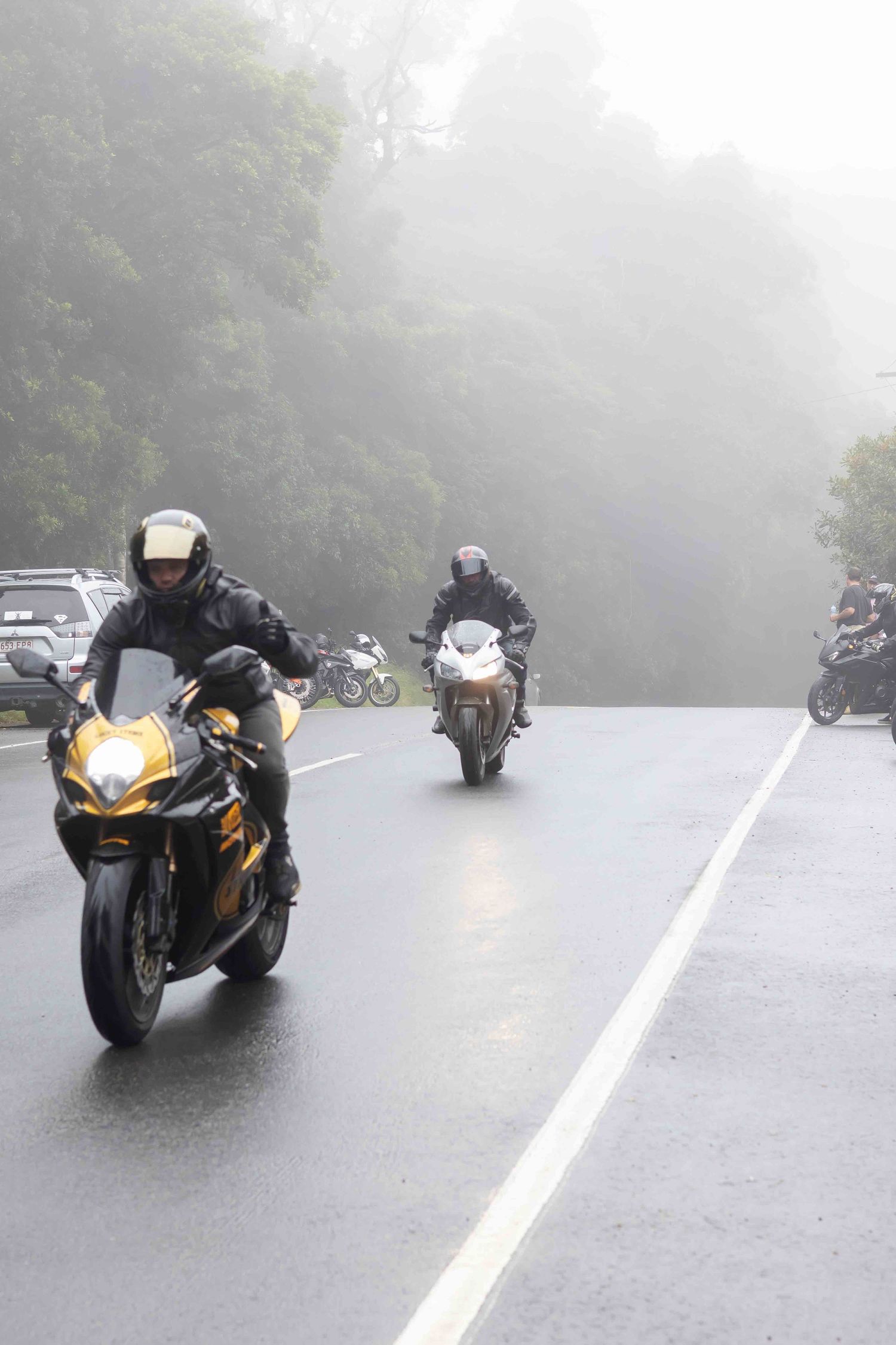 Sport bikes cruising down a foggy mountain road with yellow and black motorcycle in focus.
