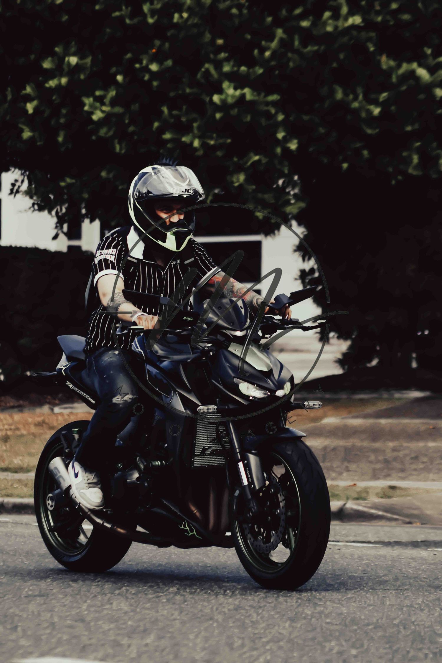 A motorcyclist wearing a white helmet rides a black sport motorcycle on a road with green trees in the background.