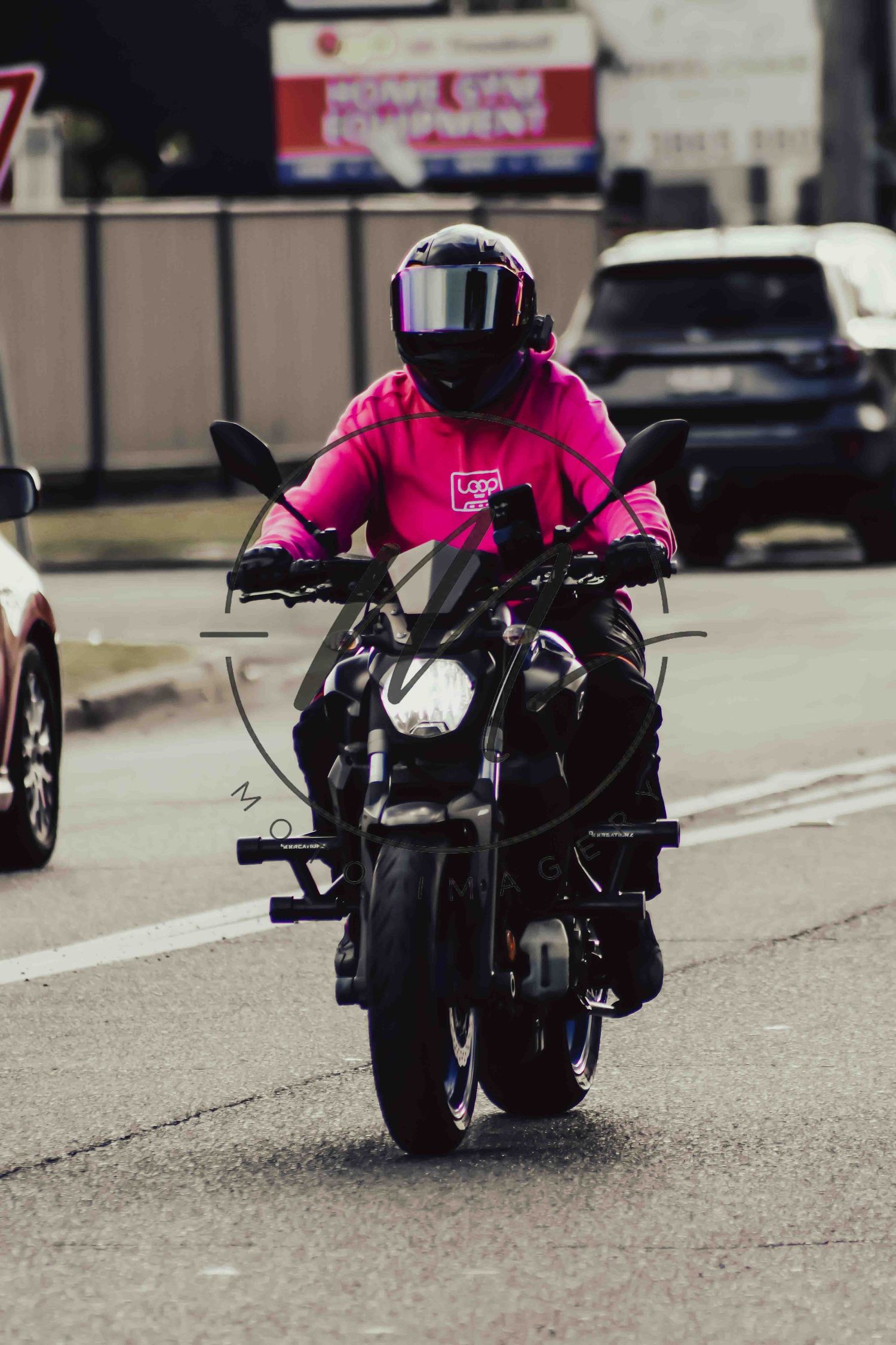 Motorcyclist in bright pink jacket and black helmet riding a dark motorcycle on a busy urban street.