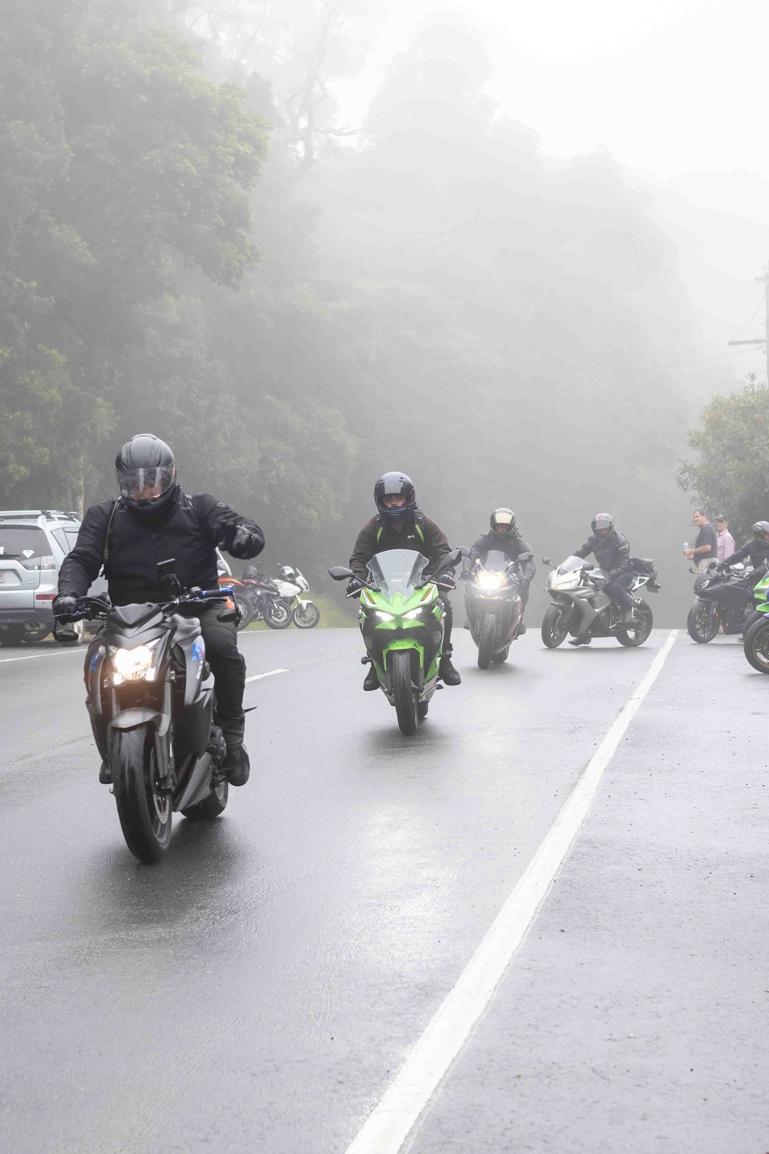 Group of motorcyclists riding through foggy mountain road conditions.