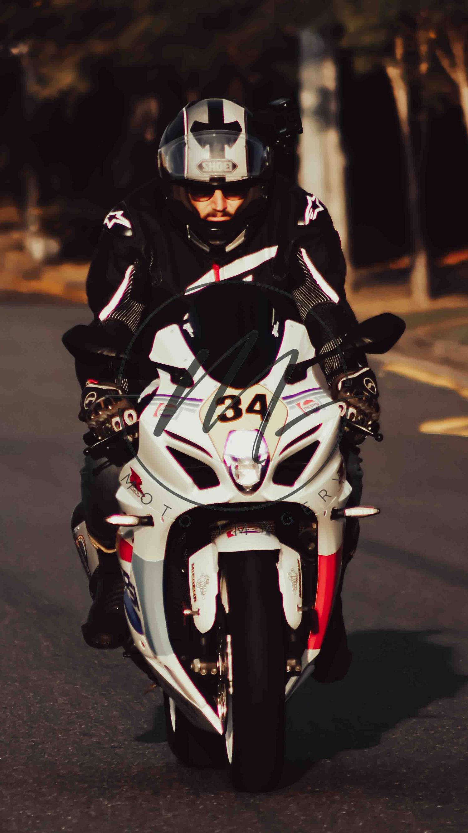 Motorcycle racer in black leather suit and helmet riding white sport bike number 34 on a road.