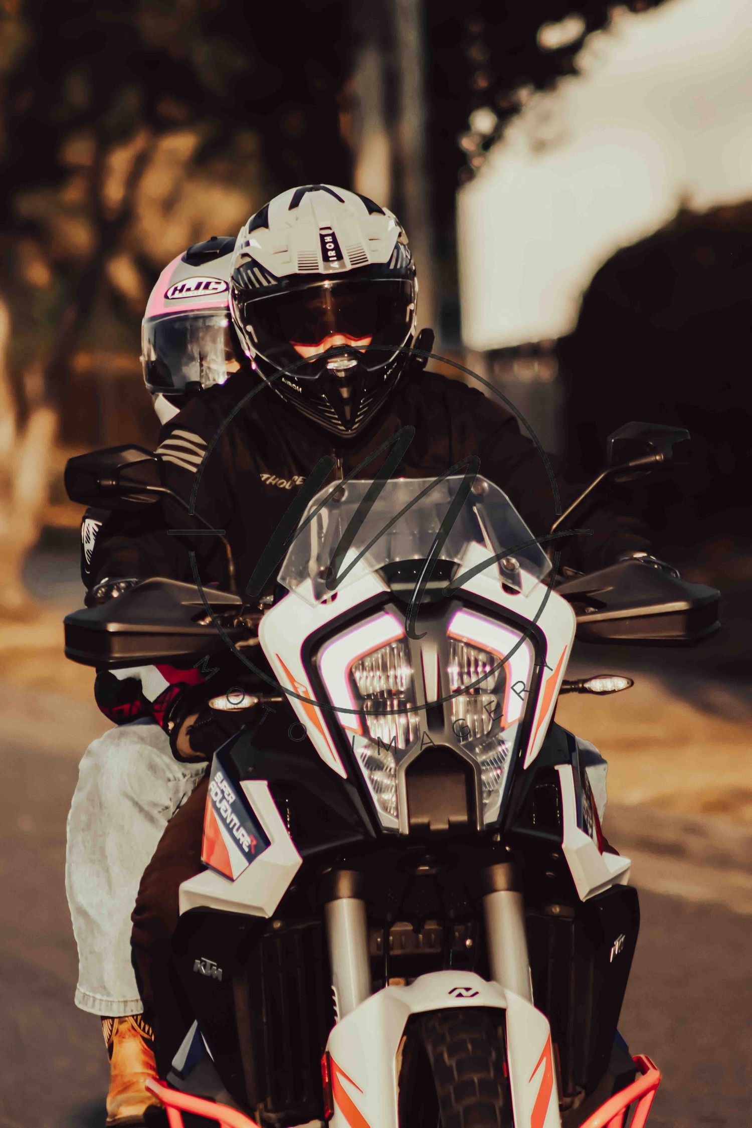 A motorcyclist in a white HJC helmet and black gear rides a KTM adventure bike on a street at golden hour.