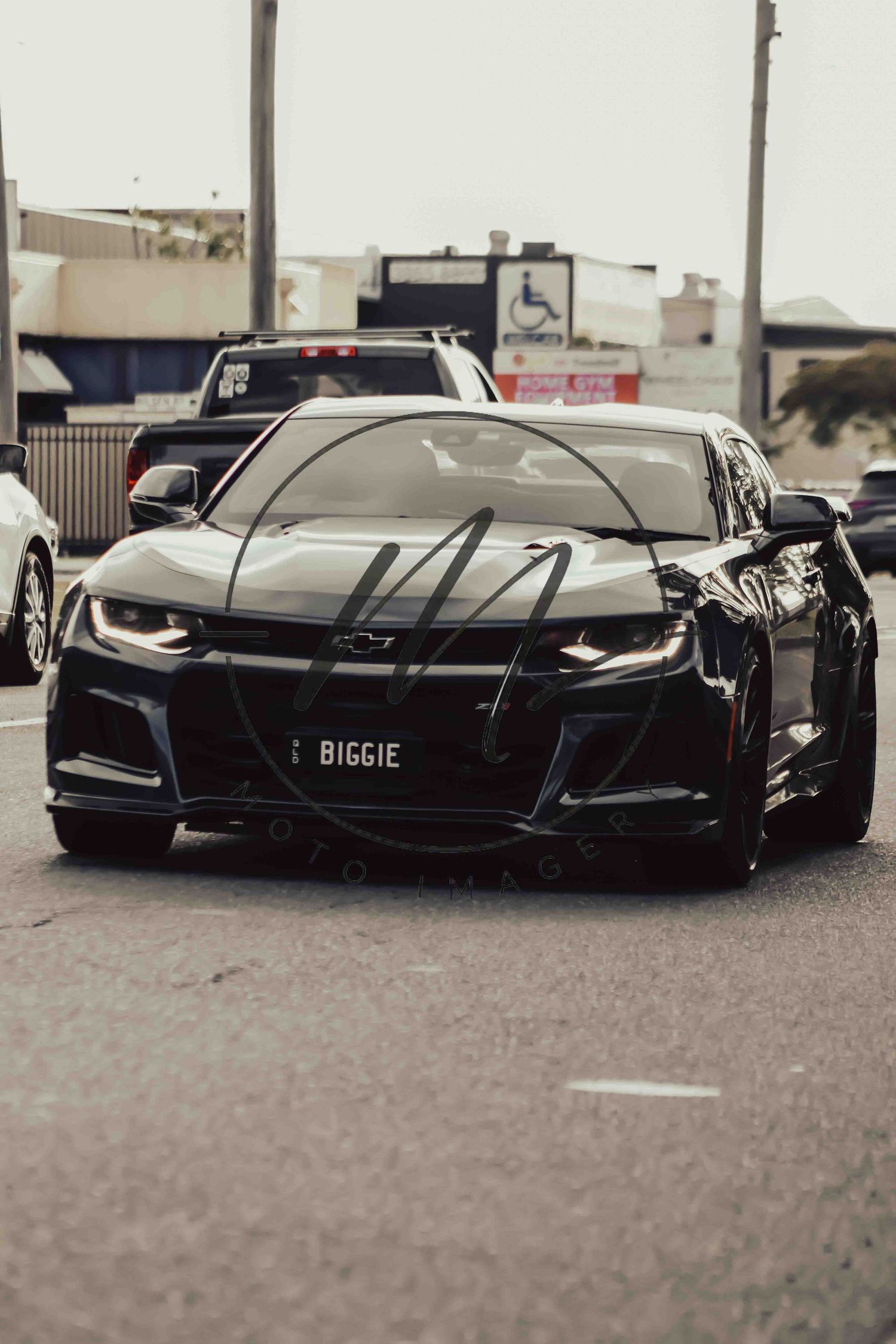 Black Chevrolet Camaro with BIGGIE license plate parked on a street, showcasing its aggressive front fascia and sleek design.