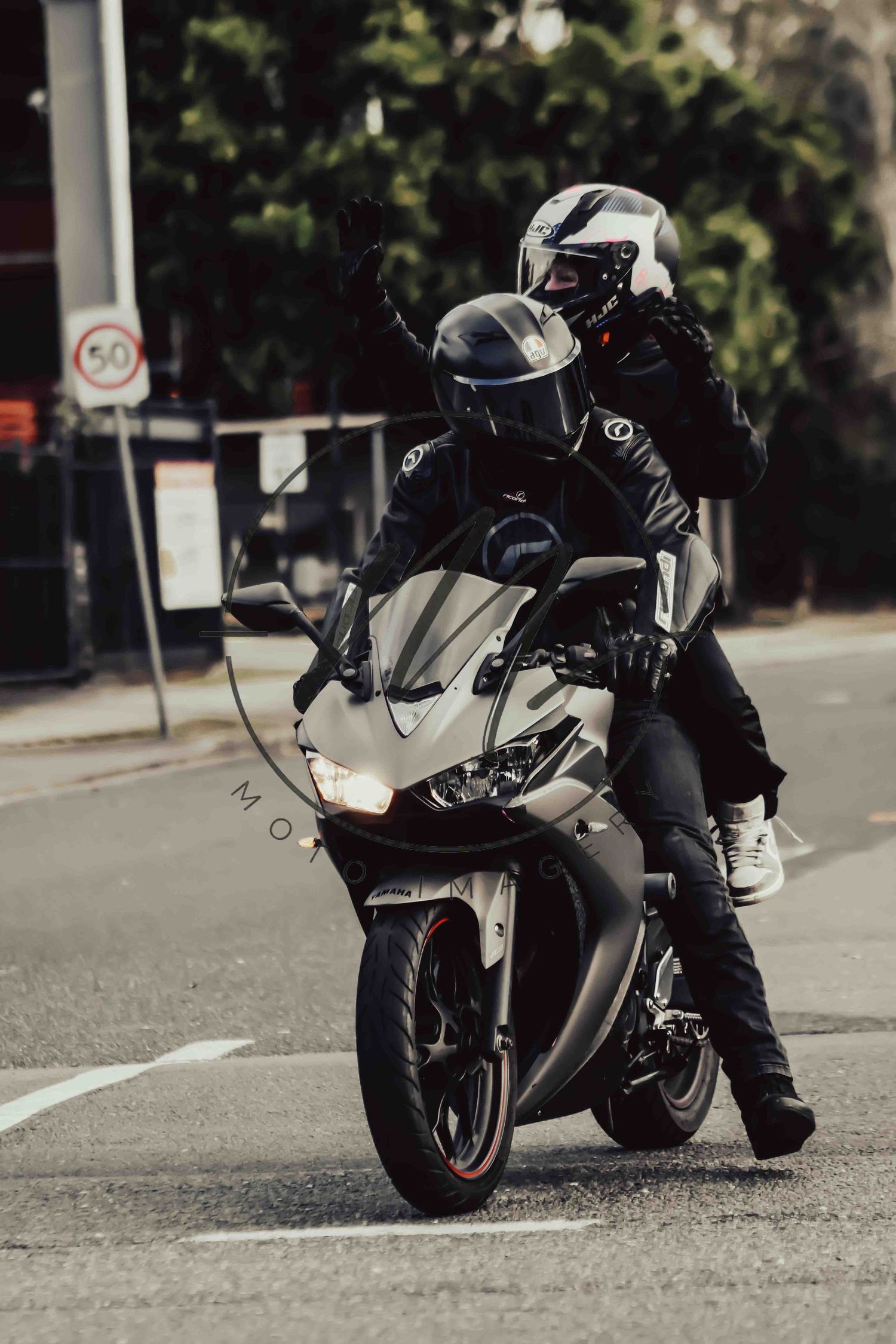 Two motorcyclists in helmets and leather jackets ride a white sport motorcycle on a city street.