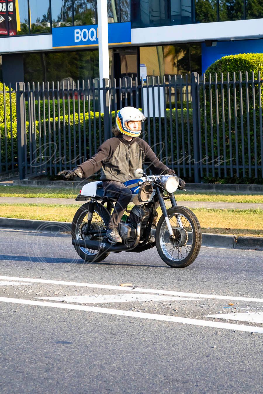 Vintage motorcycle cruising down a suburban street with business signage in the background.