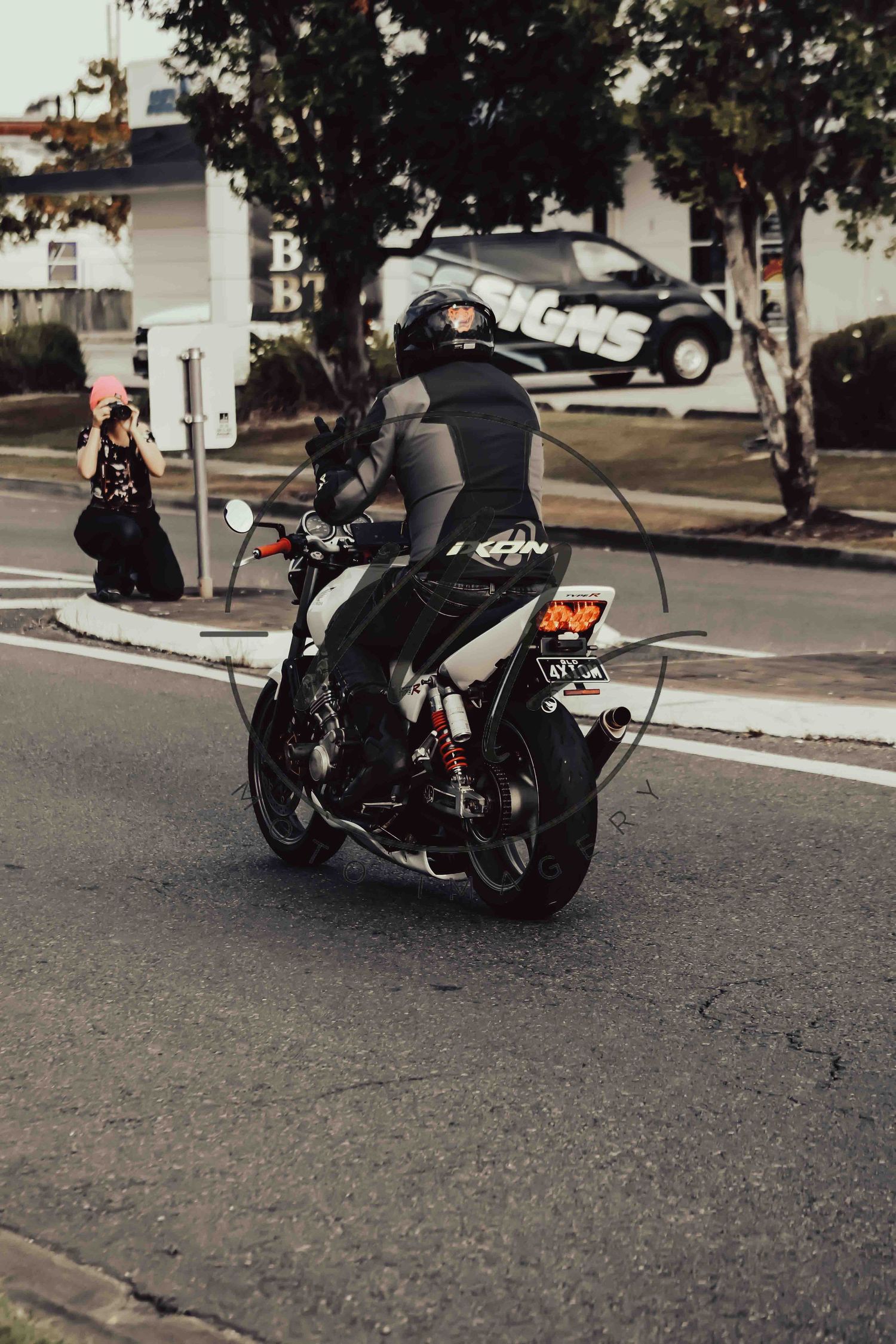 Motorcyclist in black leather gear and helmet riding a sport bike through an urban intersection.