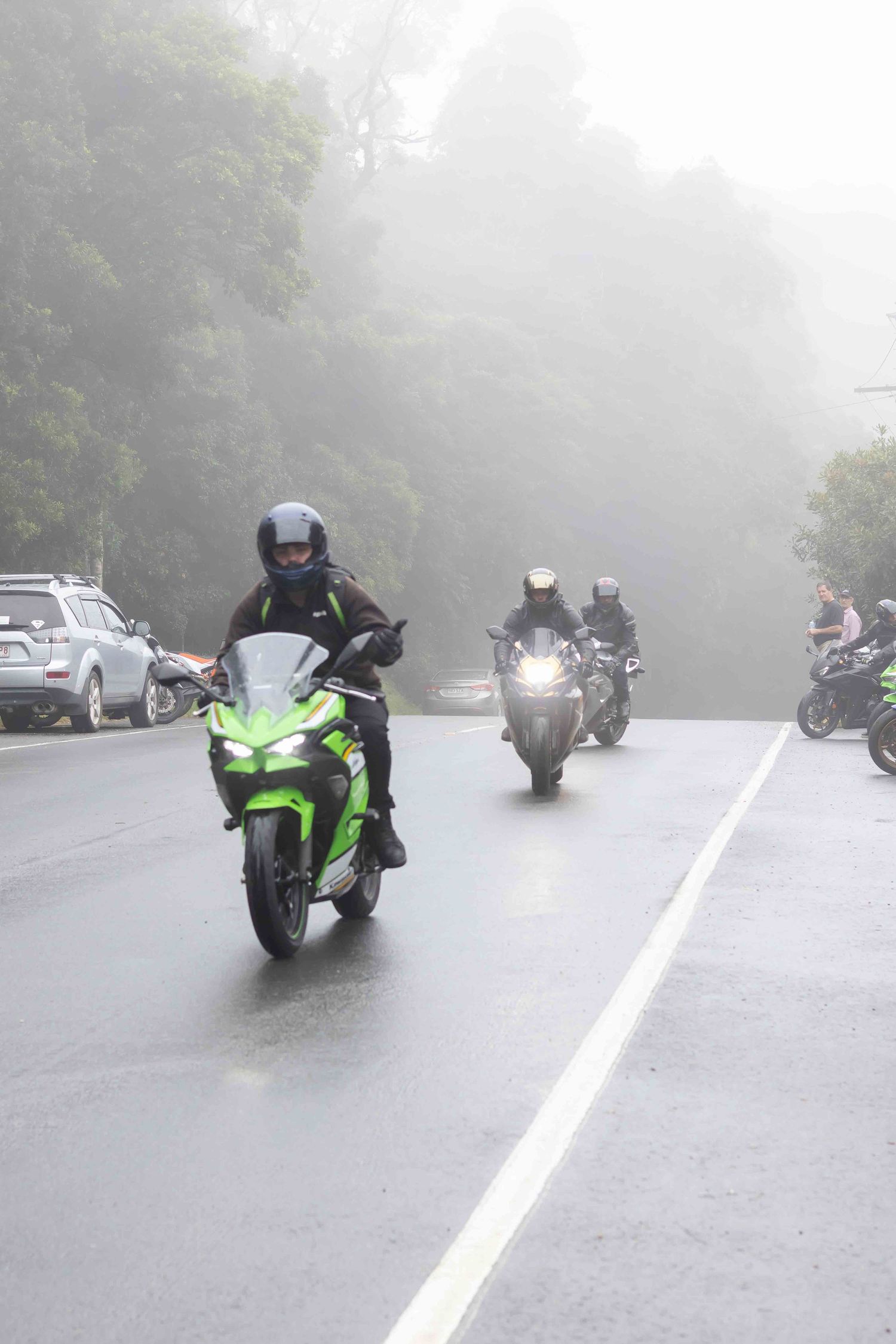 Motorcycles riding in formation on a misty road with a bright green sport bike visible.