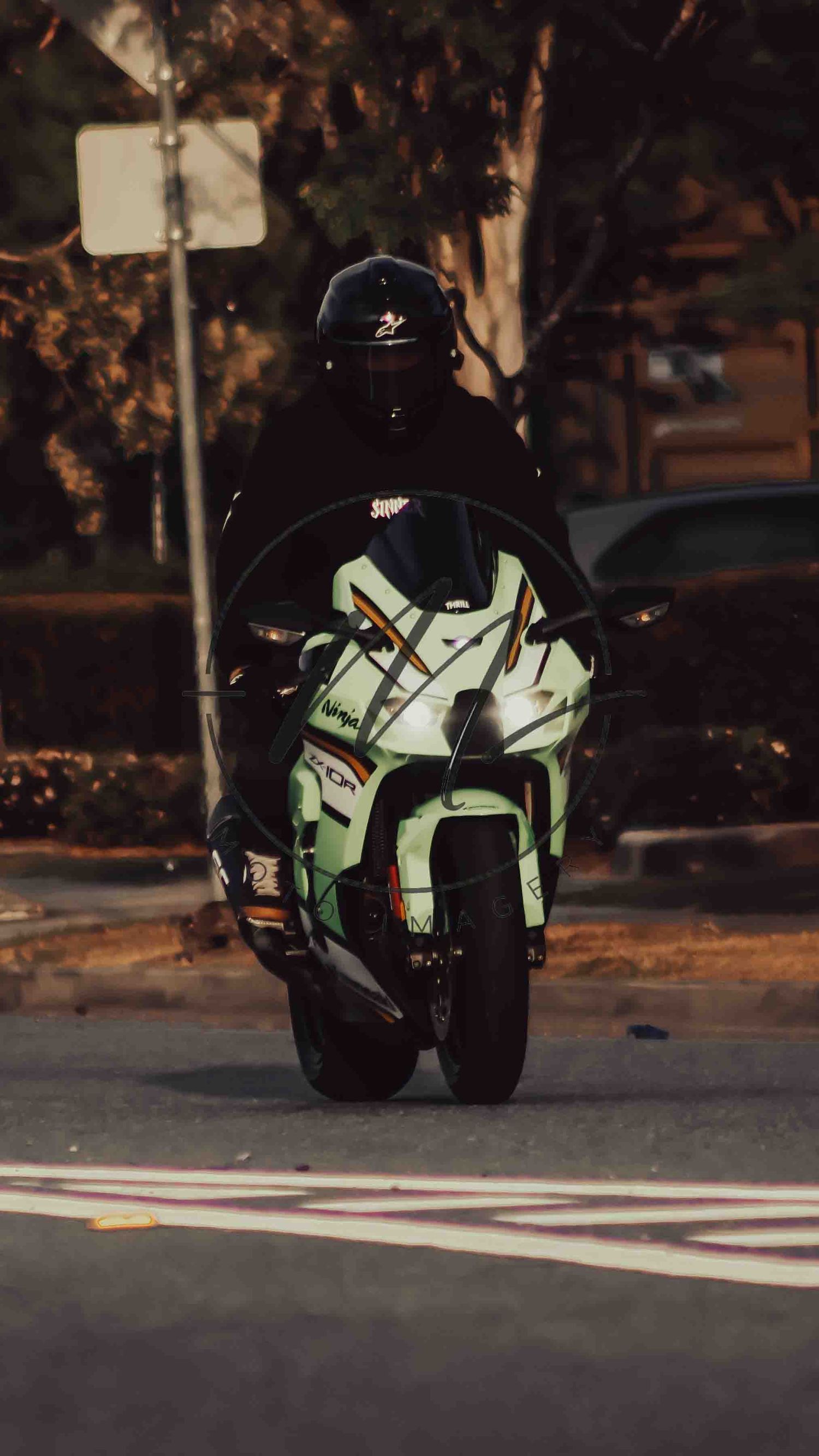 Rider in black helmet on a white and green sport motorcycle navigating a road at dusk.