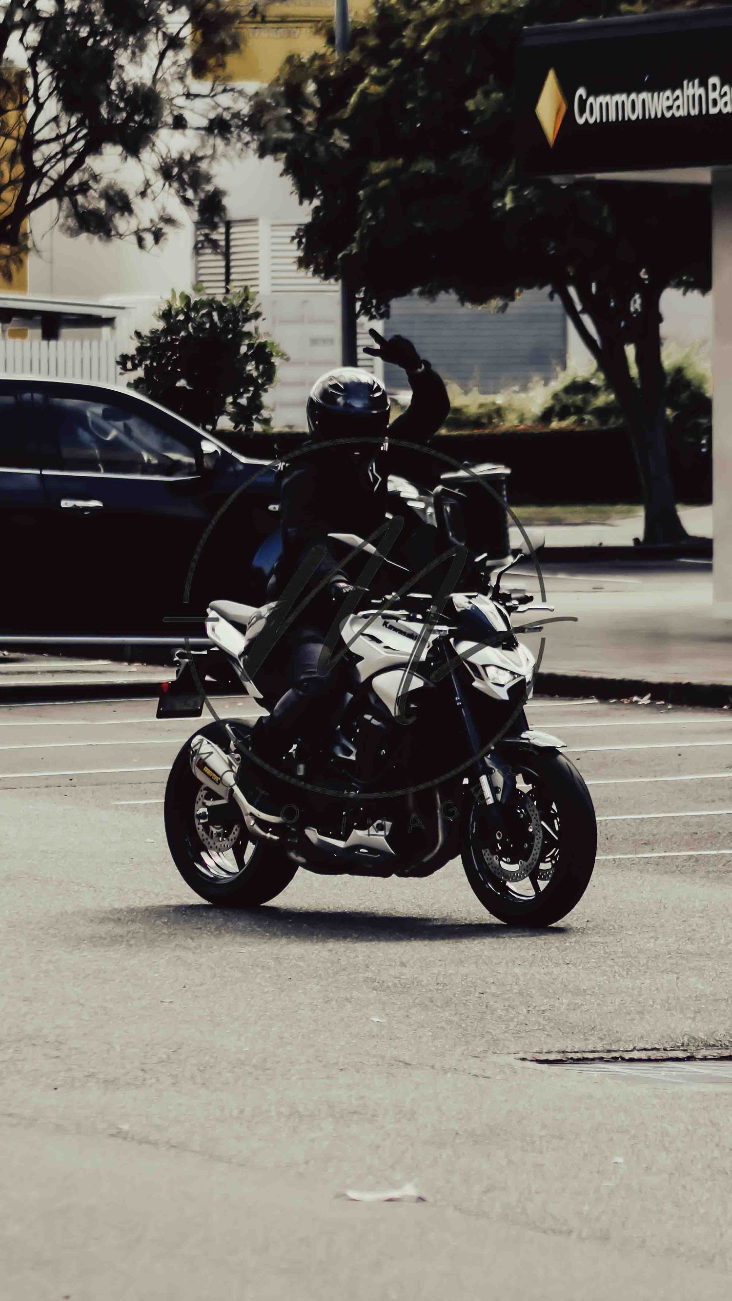 Motorcyclist riding a sport bike near a Commonwealth Bank branch on a city street.