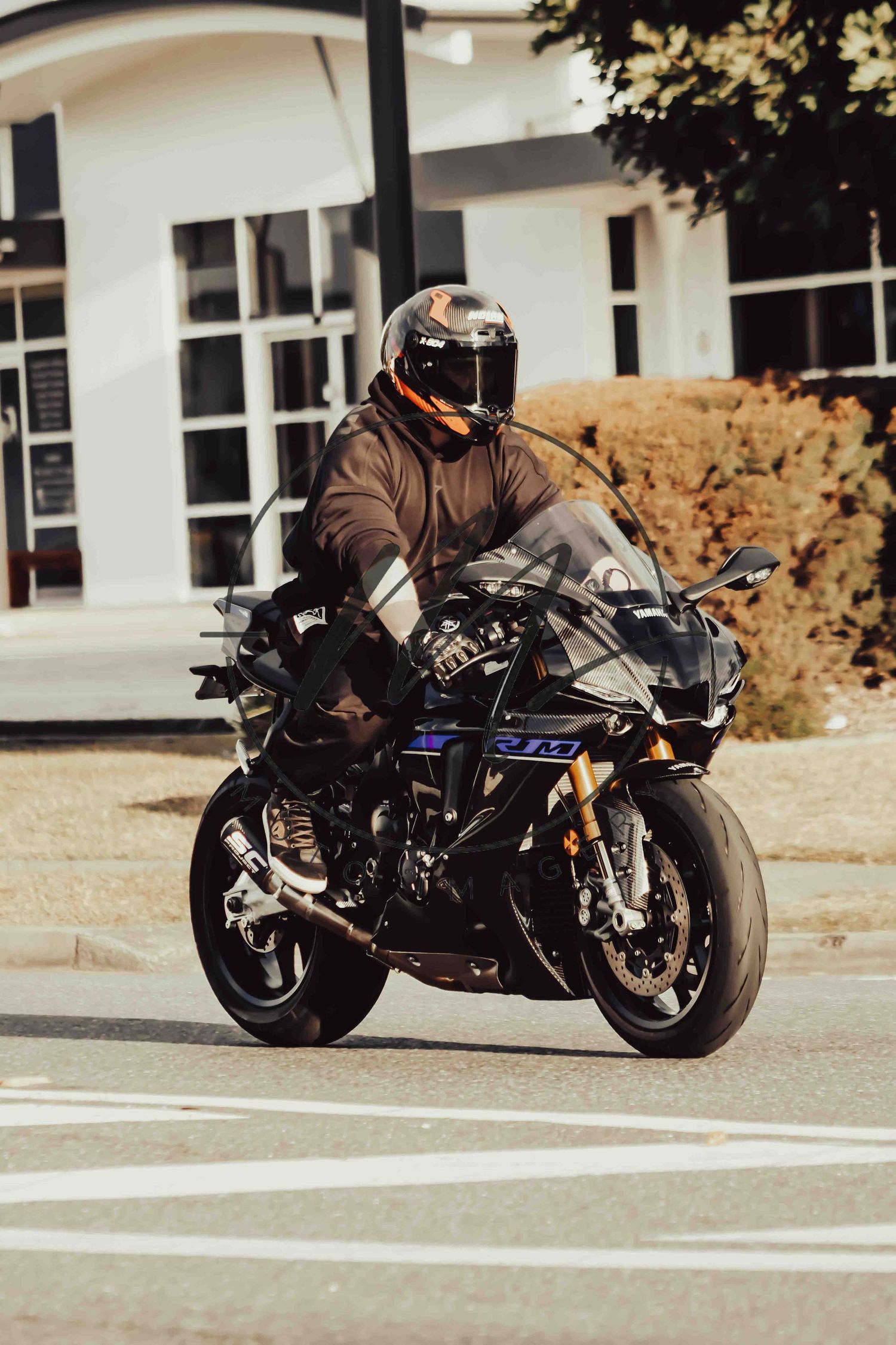 Motorcyclist in black helmet and jacket riding a sport motorcycle on a sunny urban street.