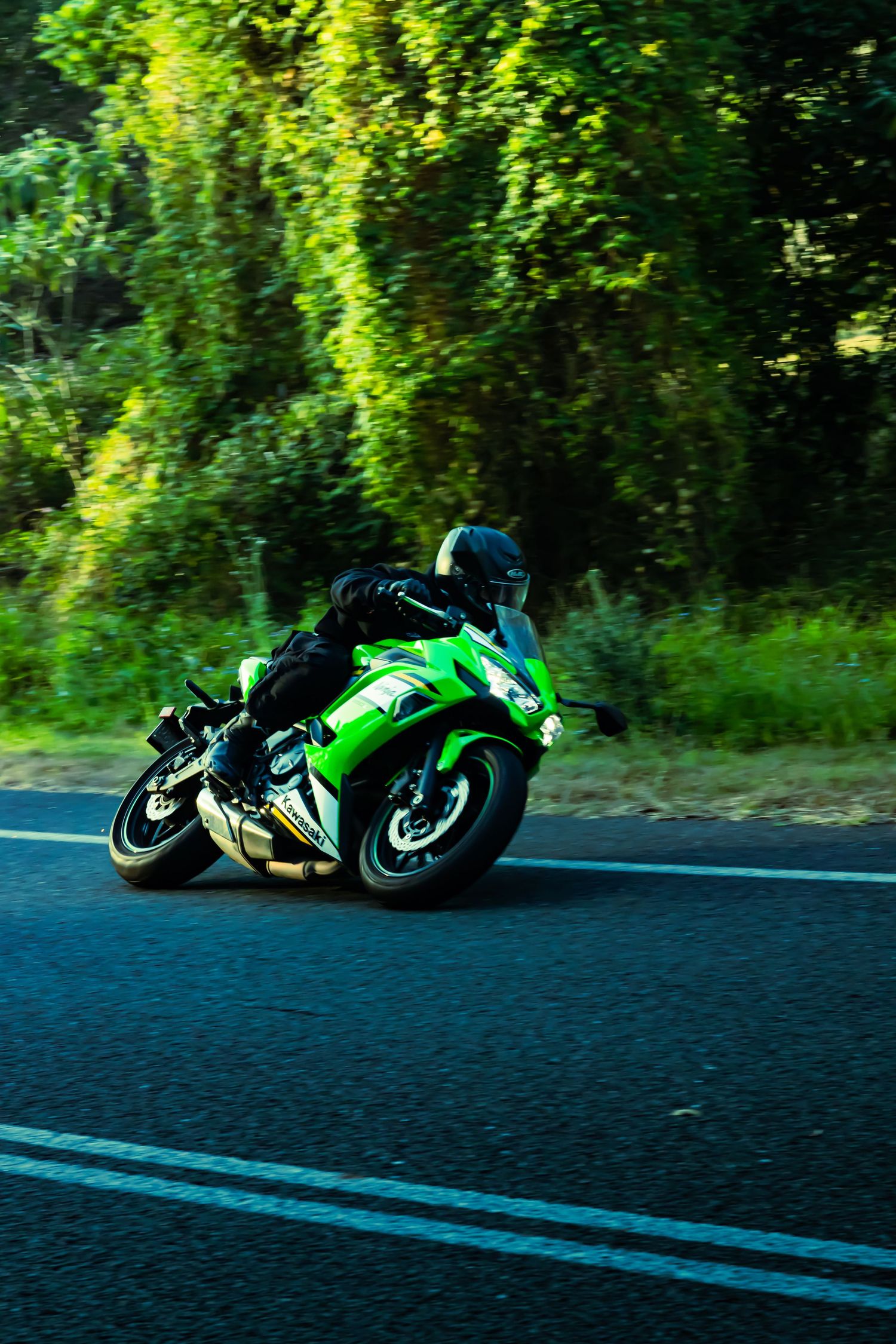 Green sportbike leaning through corner on dark asphalt road.