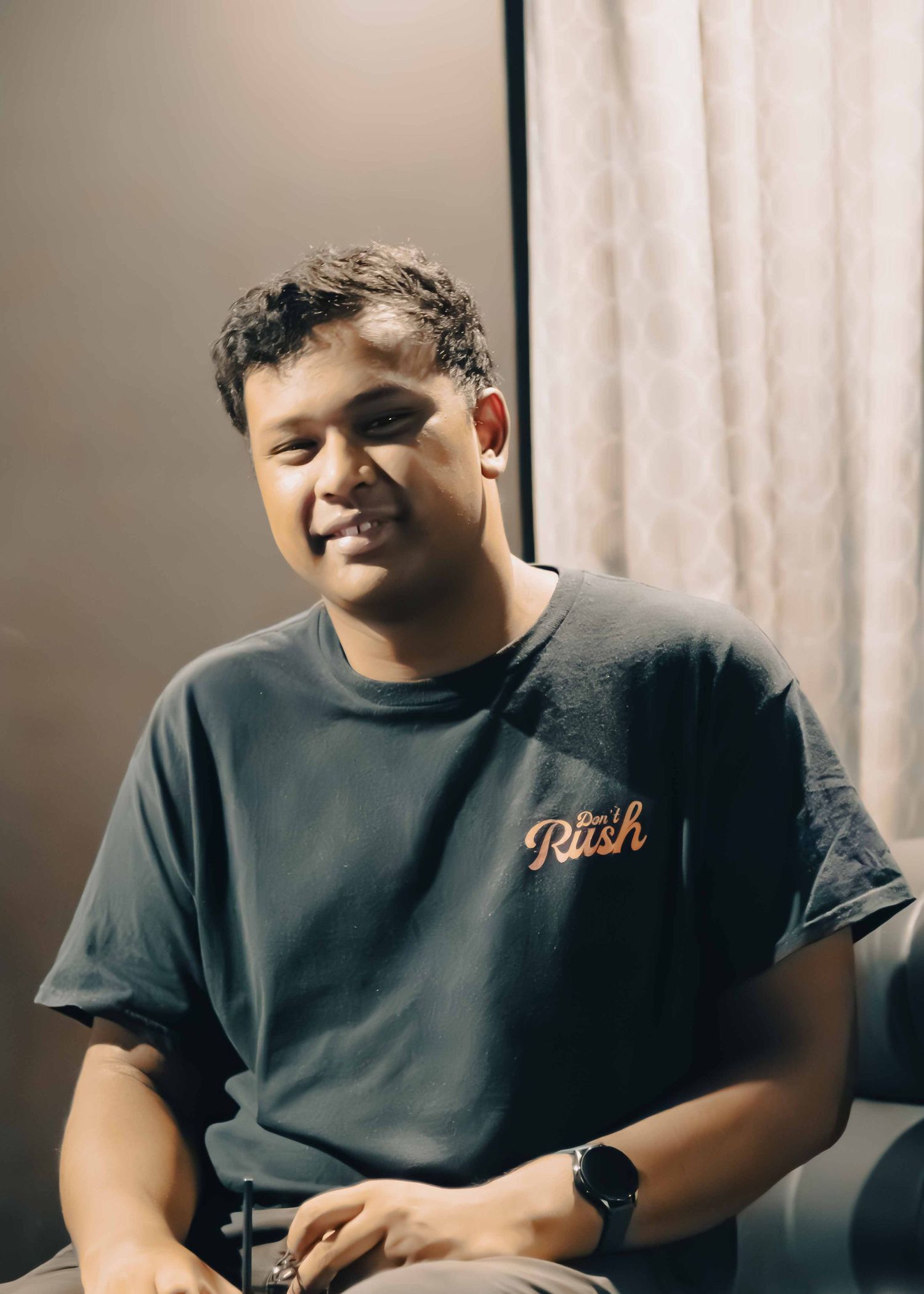 Person wearing a dark t-shirt smiles while sitting in a casual indoor setting.