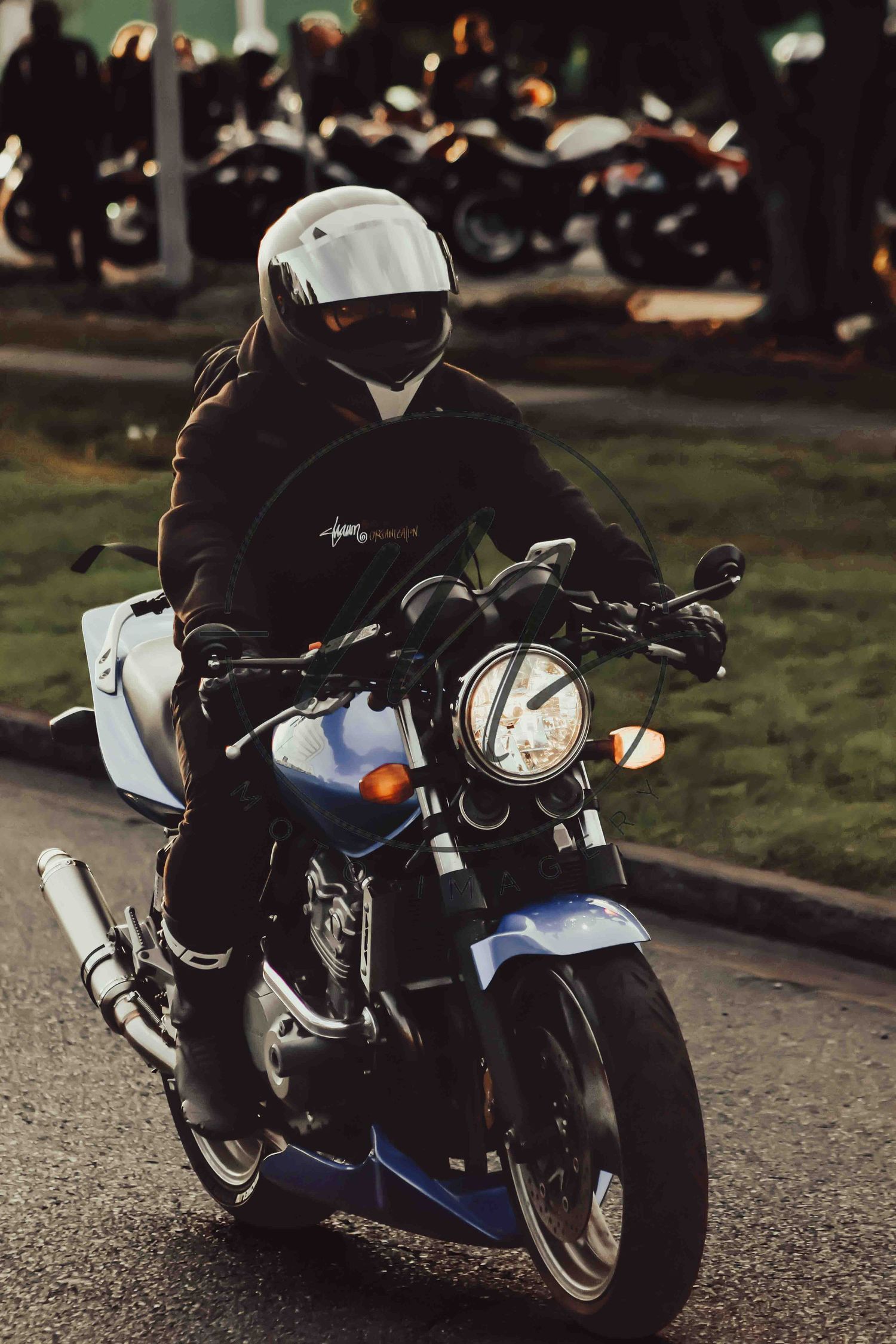 Motorcyclist in white helmet and black jacket riding a blue classic motorcycle on a street at dusk.