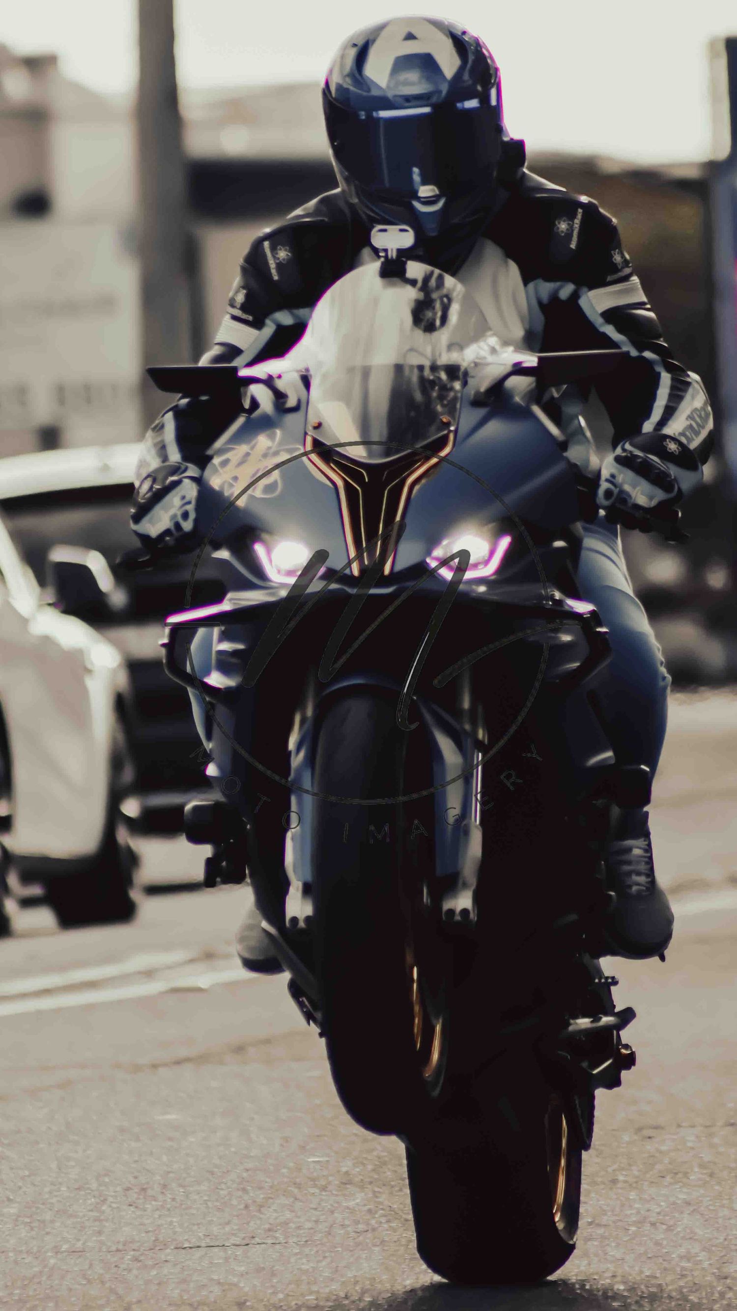 A motorcyclist in black leather gear and helmet rides a sport motorcycle with purple LED lights on a city street.