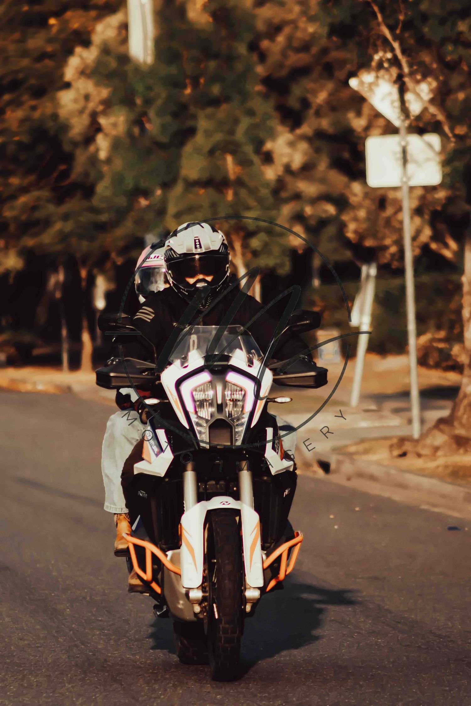 A motorcyclist in full gear rides a KTM adventure bike on a road surrounded by trees.