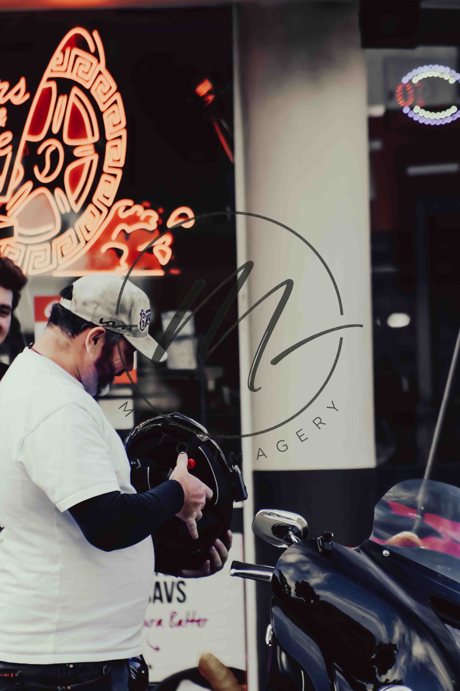 Man holding a motorcycle helmet outside a barbershop with neon signs in the background.
