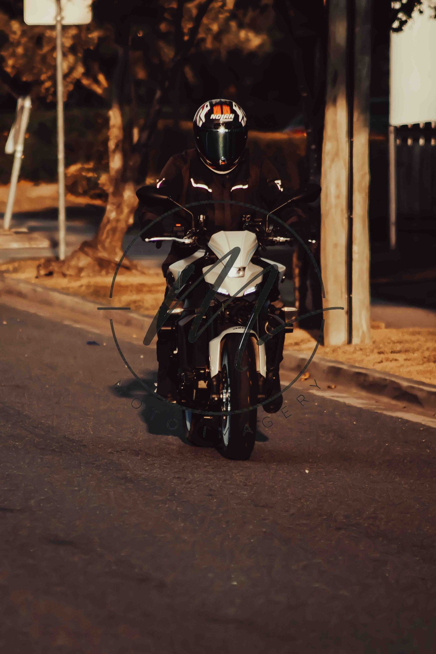 Motorcyclist in black helmet and jacket riding a sport motorcycle on a quiet urban street at dusk.