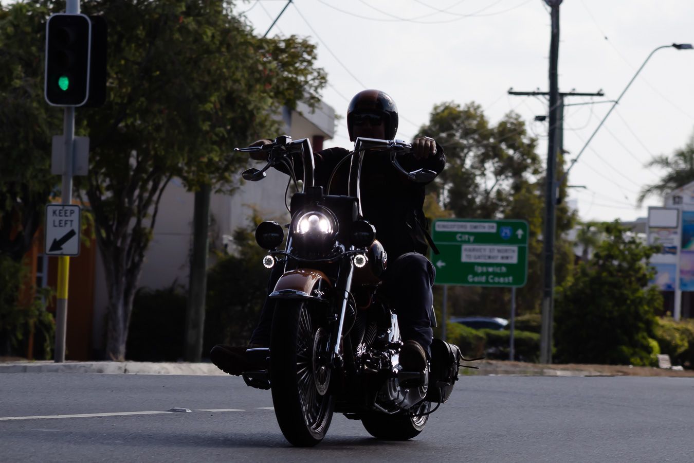 Motorcycle cruising on city street with traffic lights and trees in background.