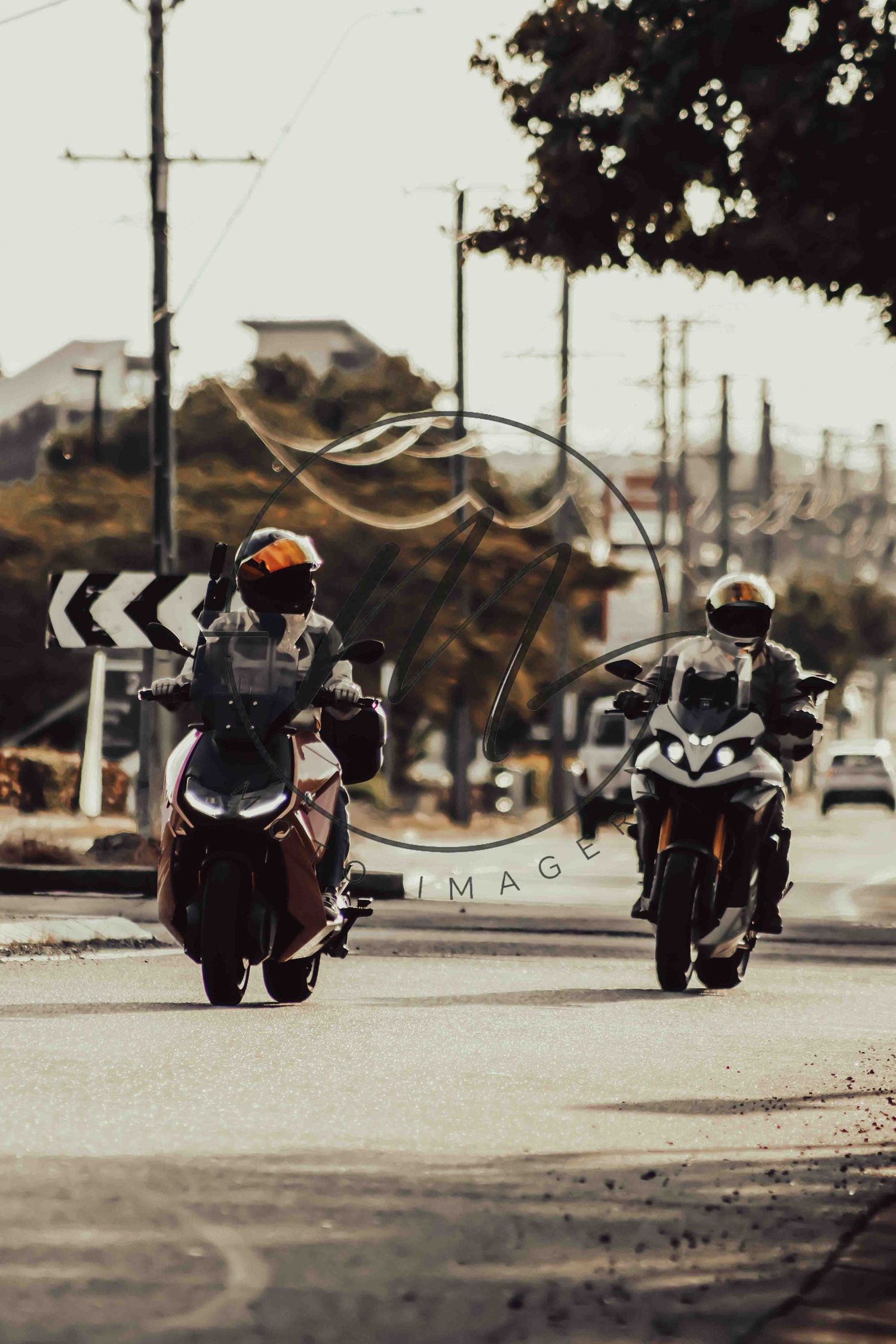 Two motorcyclists wearing helmets ride sport bikes on a road at golden hour with utility poles and trees in the background.