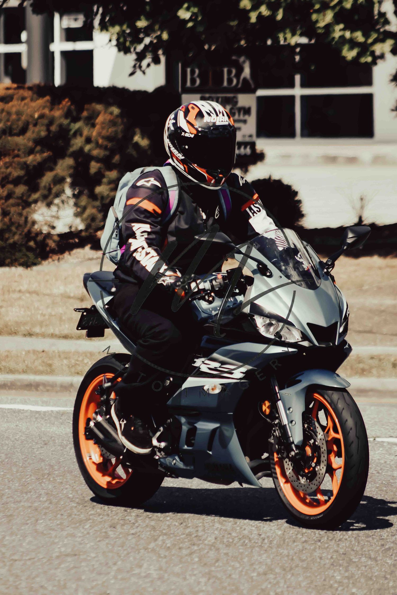 Motorcyclist in full gear and helmet riding a KTM RC sport bike with orange wheels on a city street.