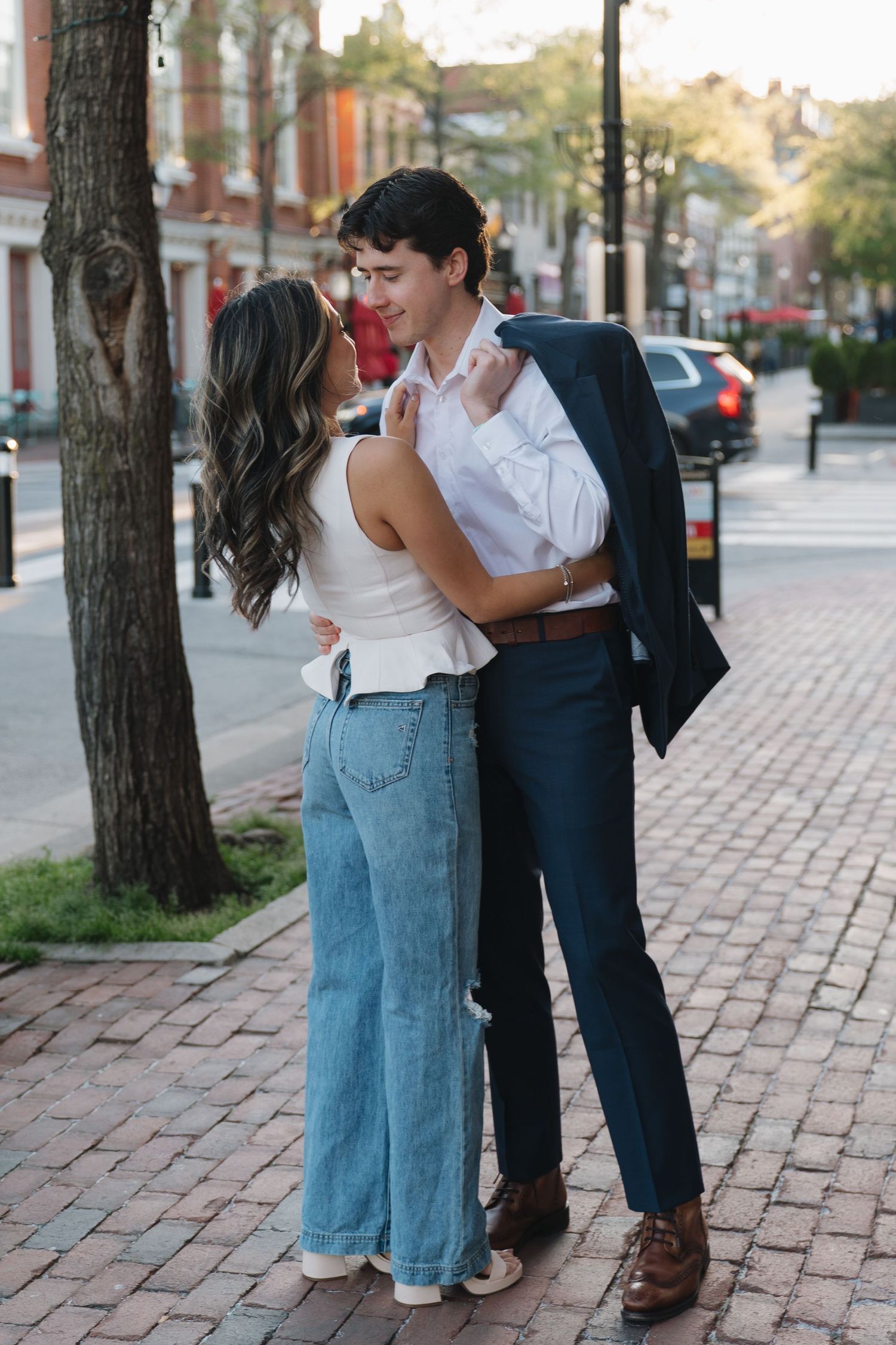 Romantic couple embracing and gazing at each other on a brick sidewalk in a quaint town.