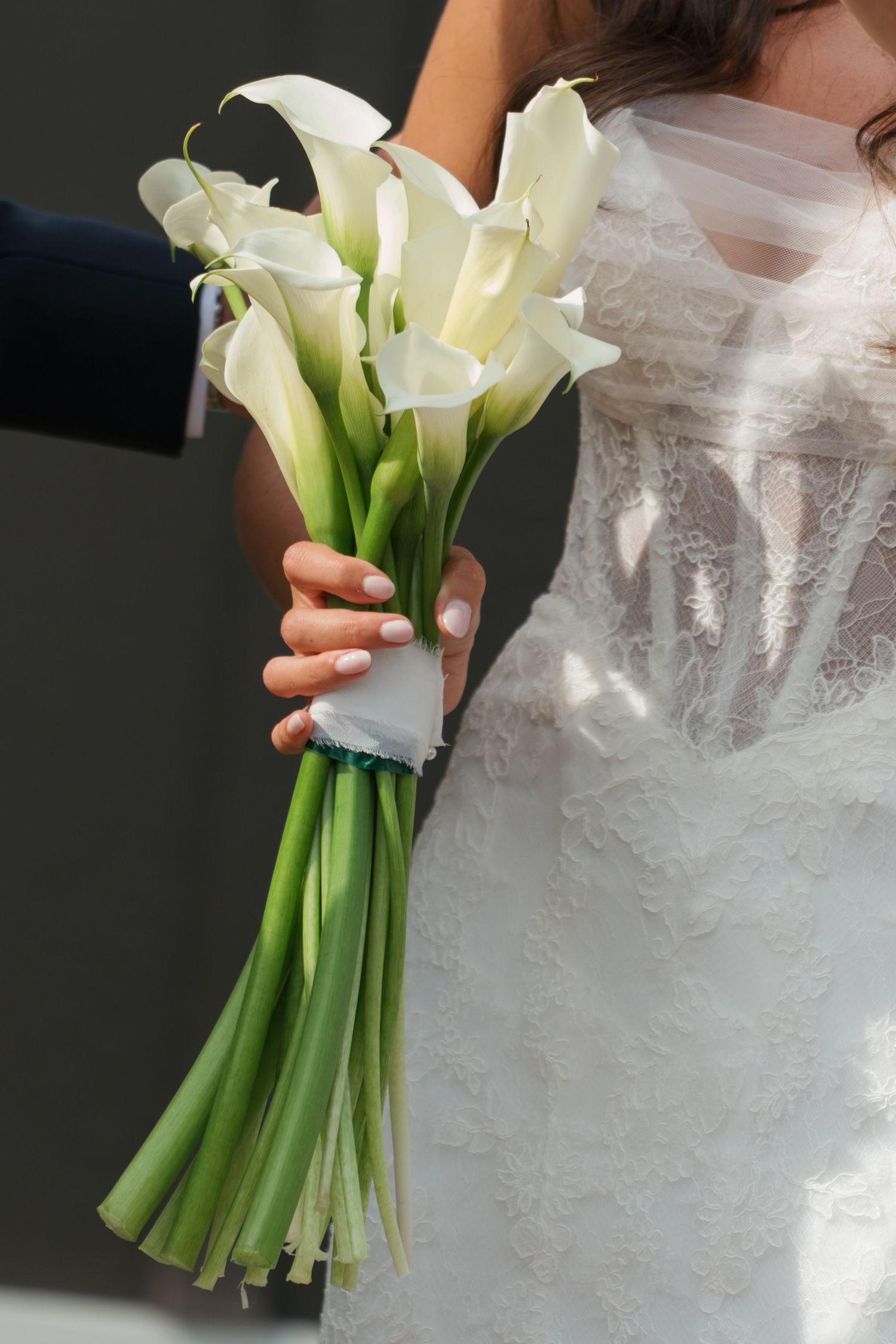 Bride in lace wedding gown holding elegant white calla lily bouquet on wedding day.