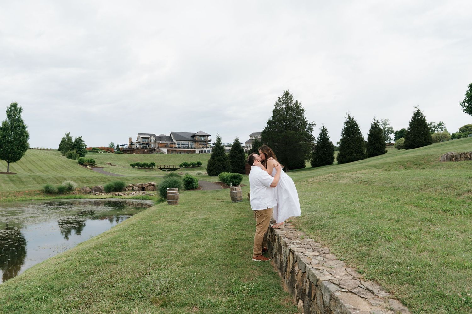 Couple sharing a tender moment near a pond on a lush green hillside landscape.
