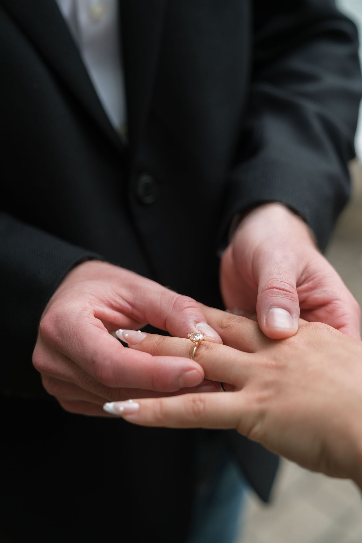 Groom placing a gold engagement ring on brides hand with white manicured nails.