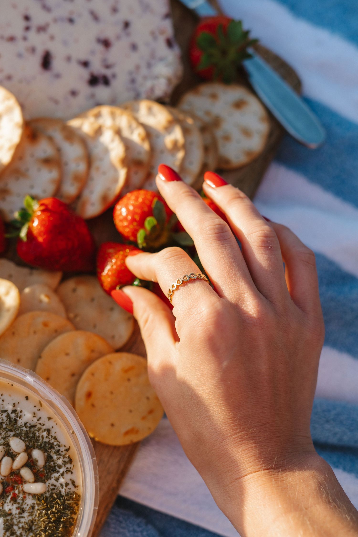 Close-up of a hand with a gold ring reaching for strawberries on a charcuterie board with crackers.