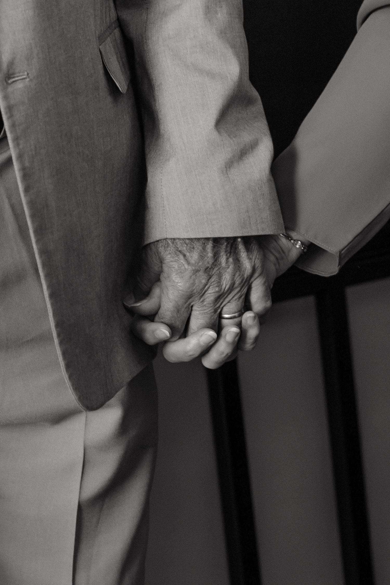 Black and white close-up of an elderly couple holding hands in formal attire.