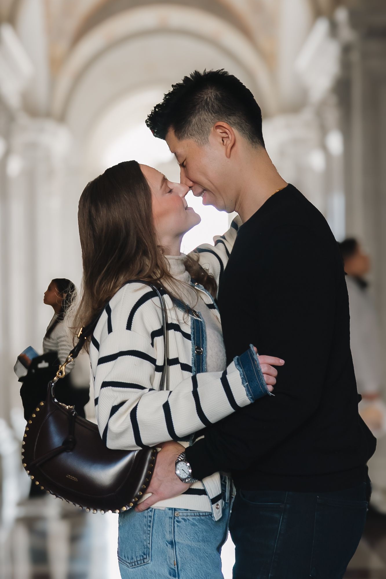 Couple sharing a romantic moment, leaning in for a kiss in an elegant arched hallway.