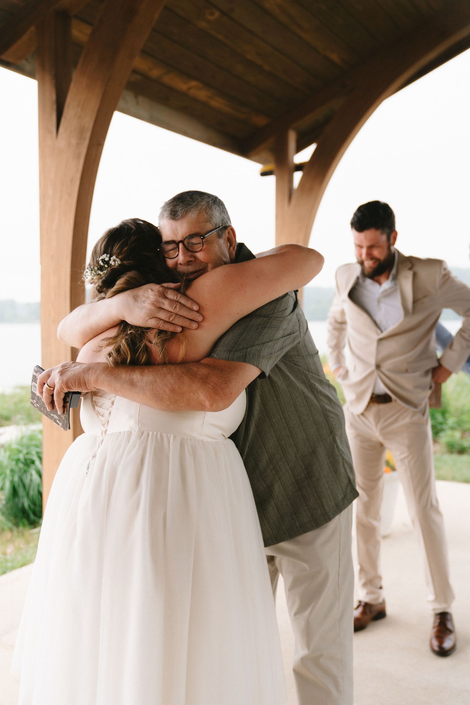 Emotional bride hugging father-in-law under a wooden pavilion at a private residence in Annapolis, Maryland.