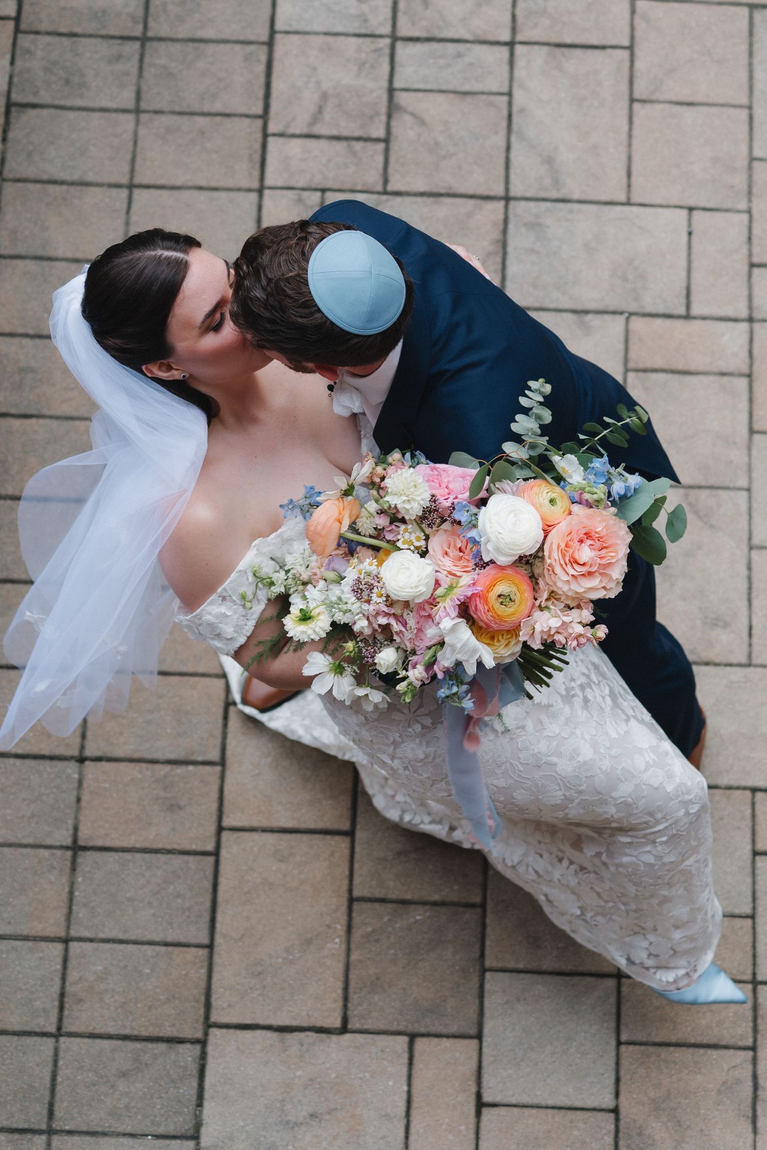 Aerial view of bride and groom sharing a romantic dip kiss with a colorful spring bouquet.