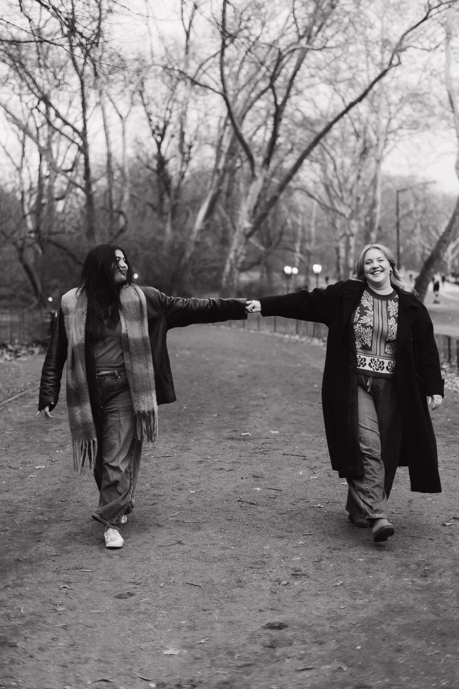 Black and white photo of two women holding hands while walking apart on a park path.
