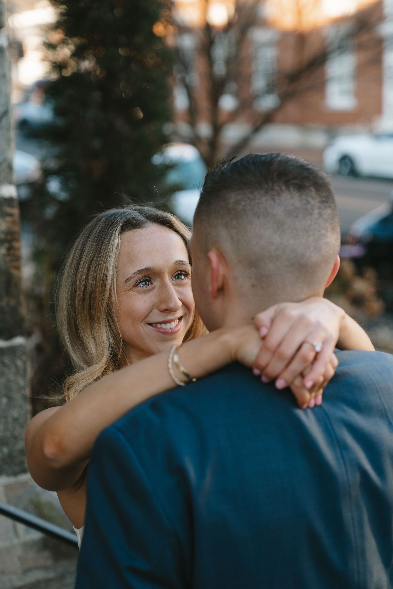 Smiling blonde woman hugging her partner during an outdoor engagement photo session.