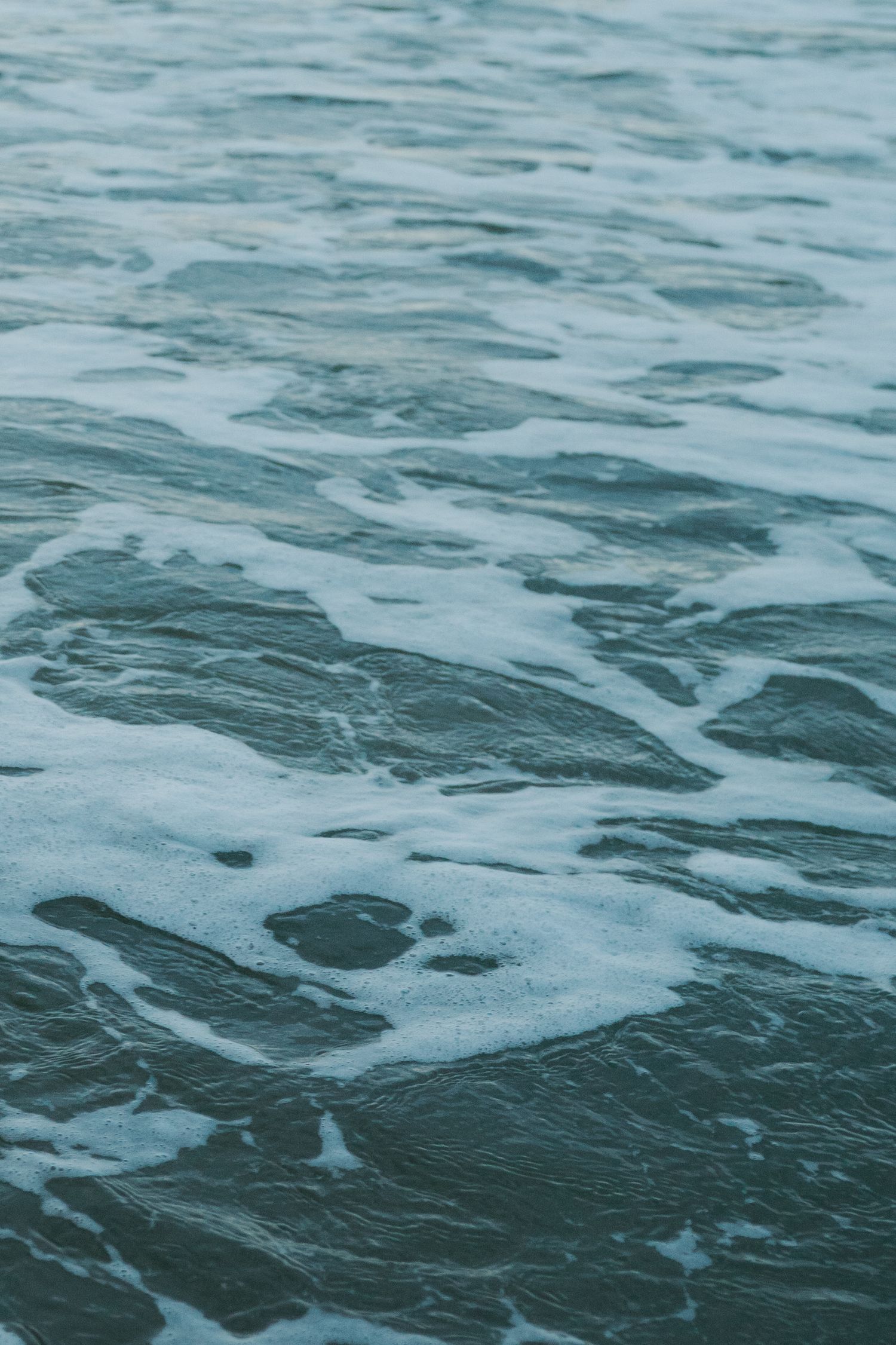 Close-up of dark teal ocean water with white sea foam creating abstract texture pattern.