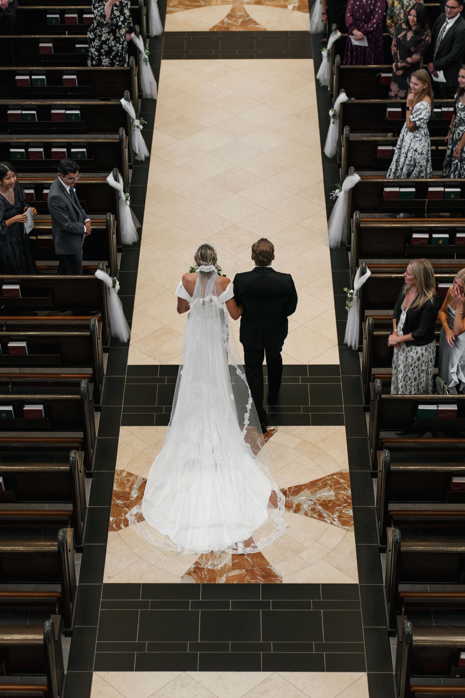 Aerial view of bride walking down church aisle in cathedral-length veil with escort.