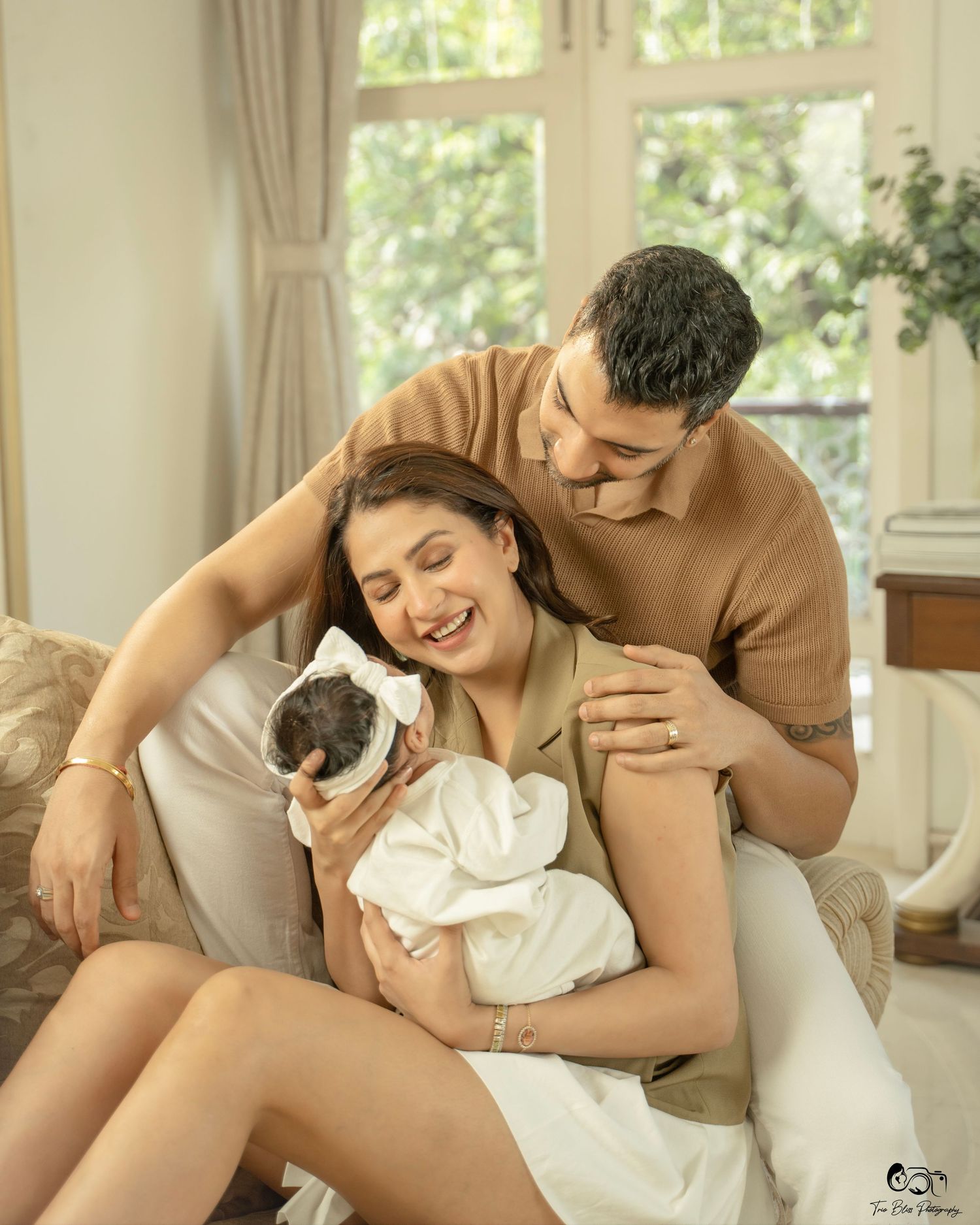Happy couple smiling at their newborn baby during a professional family portrait session indoors.