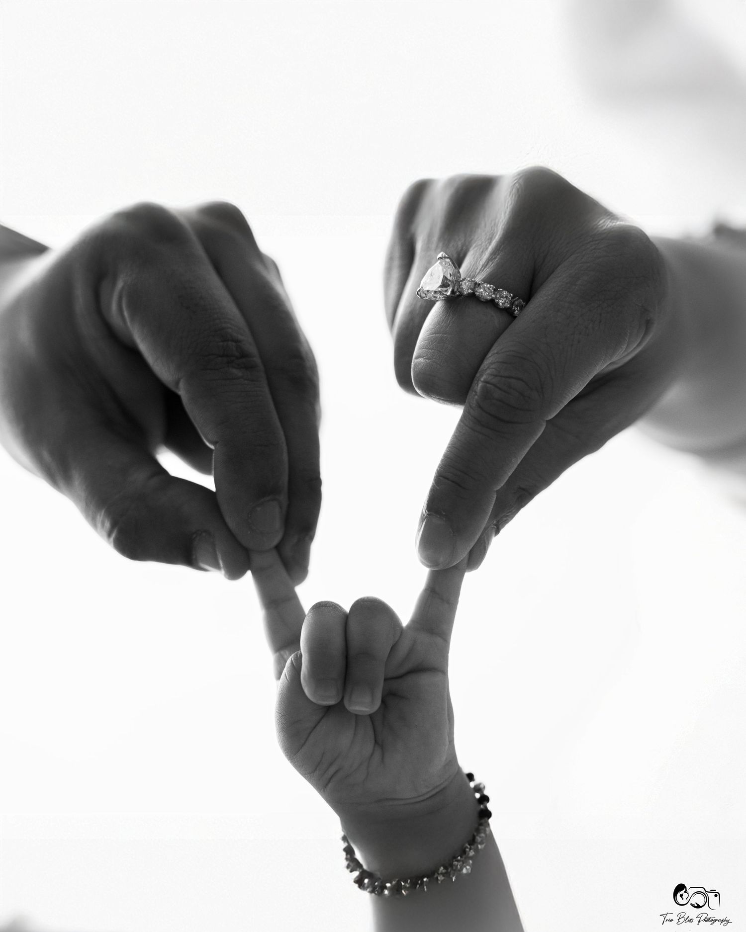 Black and white photo of two parents and a baby holding fingers together, symbolizing family love and new beginnings.