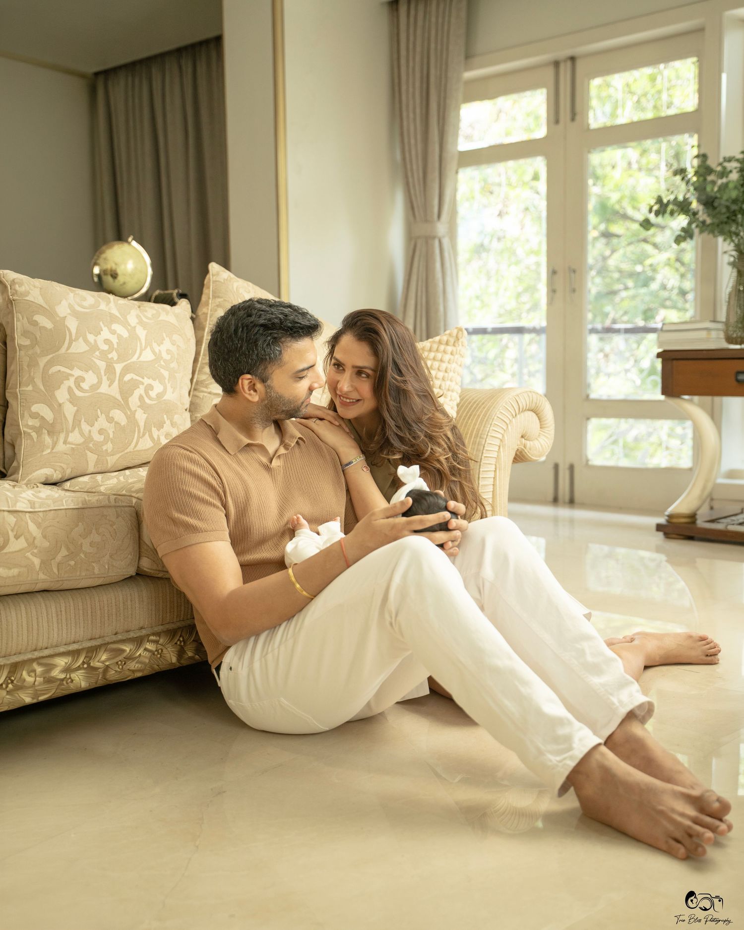 Couple sitting on floor leaning against sofa, sharing a tender moment in an elegant bright living room.